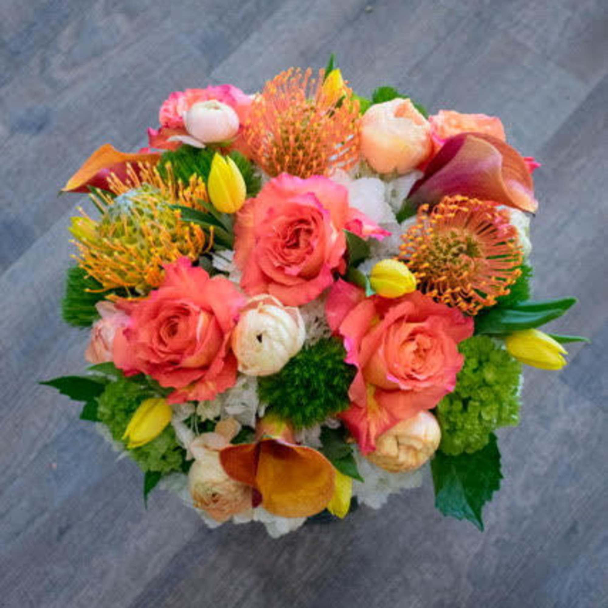 Round bouquet of coral roses, orange blooms, and yellow tulips