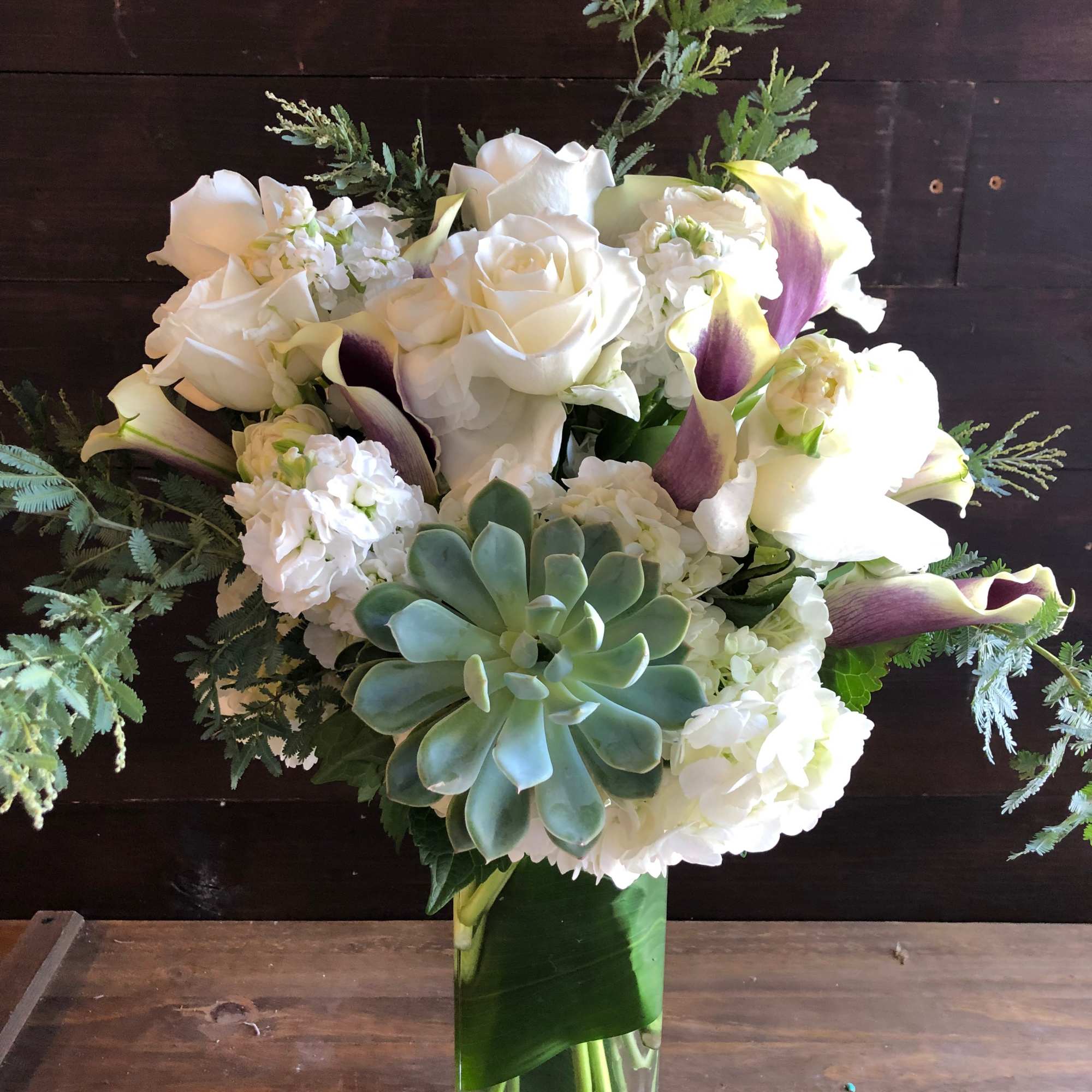 White roses and calla lilies in a tall glass vase with a succulent accent