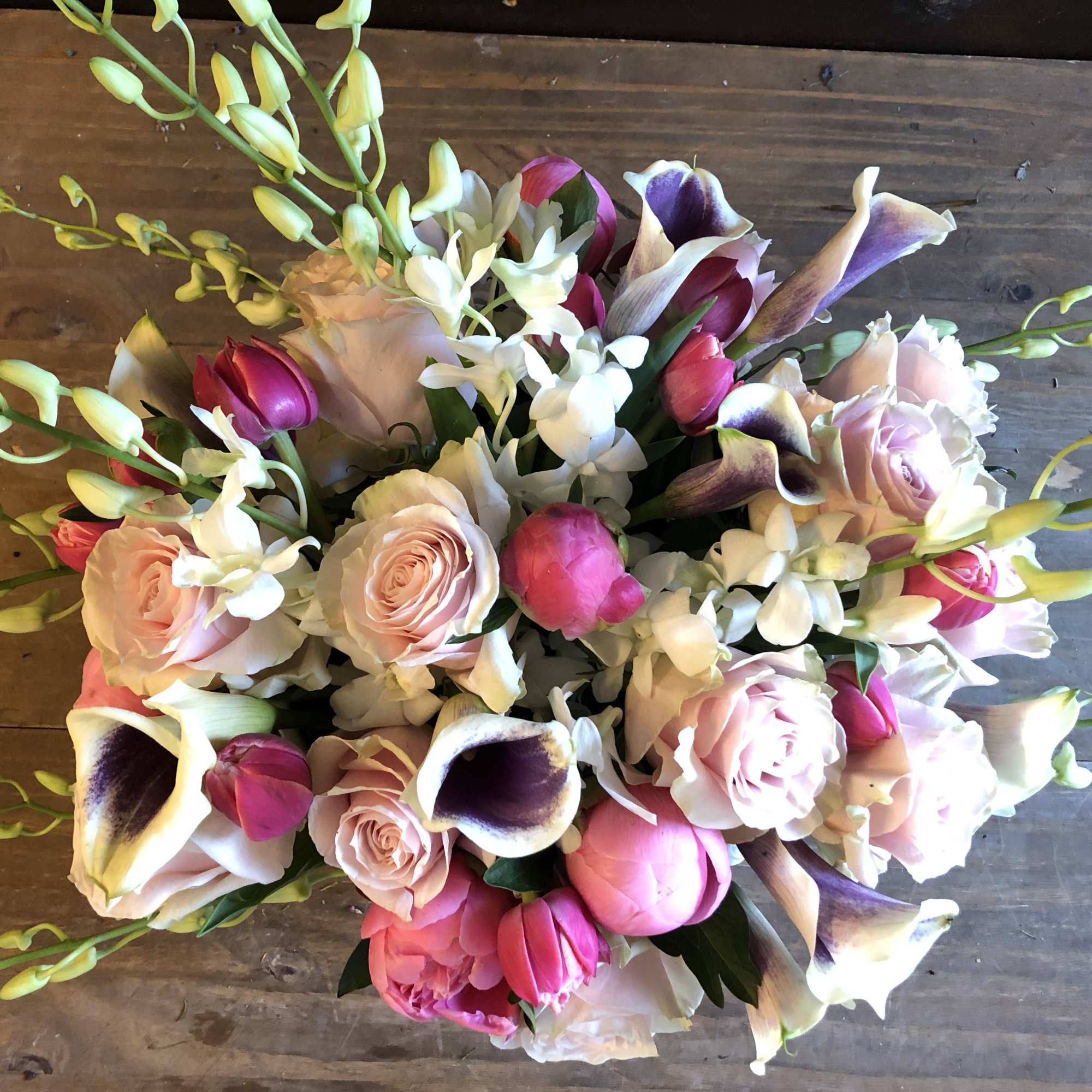 Bouquet of pink roses, calla lilies, and white orchids on a wooden surface