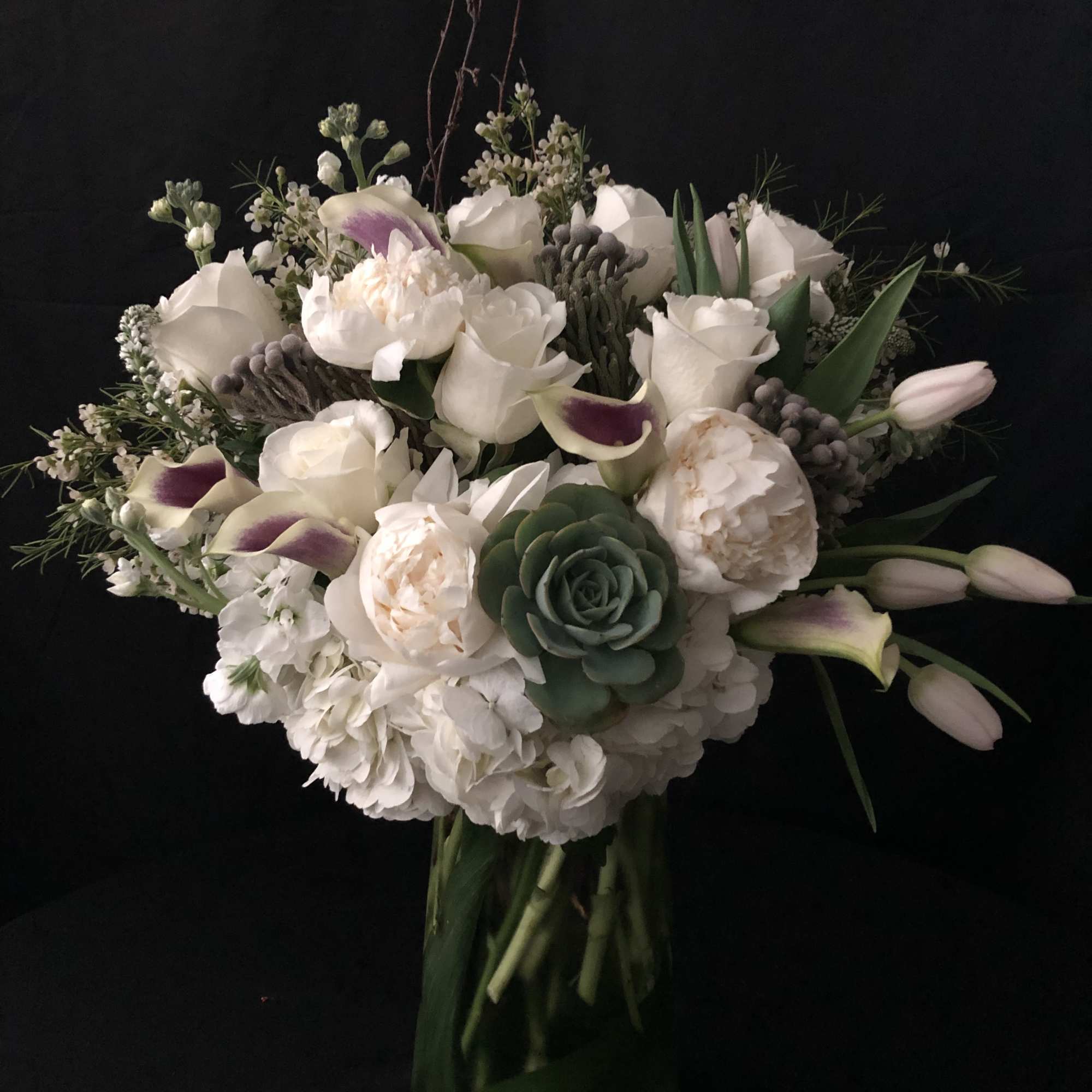 White floral bouquet with calla lilies, roses, and a green succulent in a glass vase