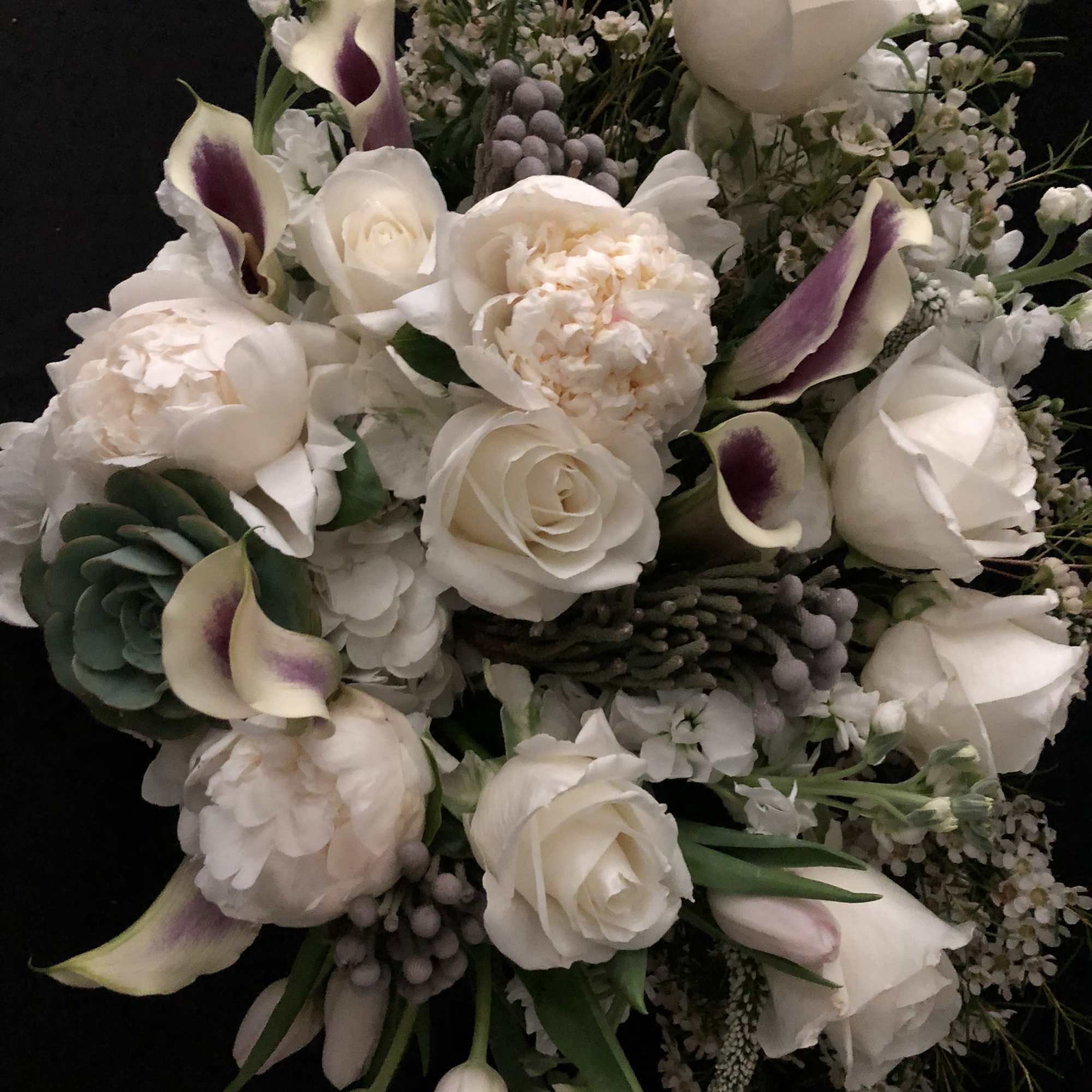 White bouquet with roses, calla lilies, and peonies on a dark background