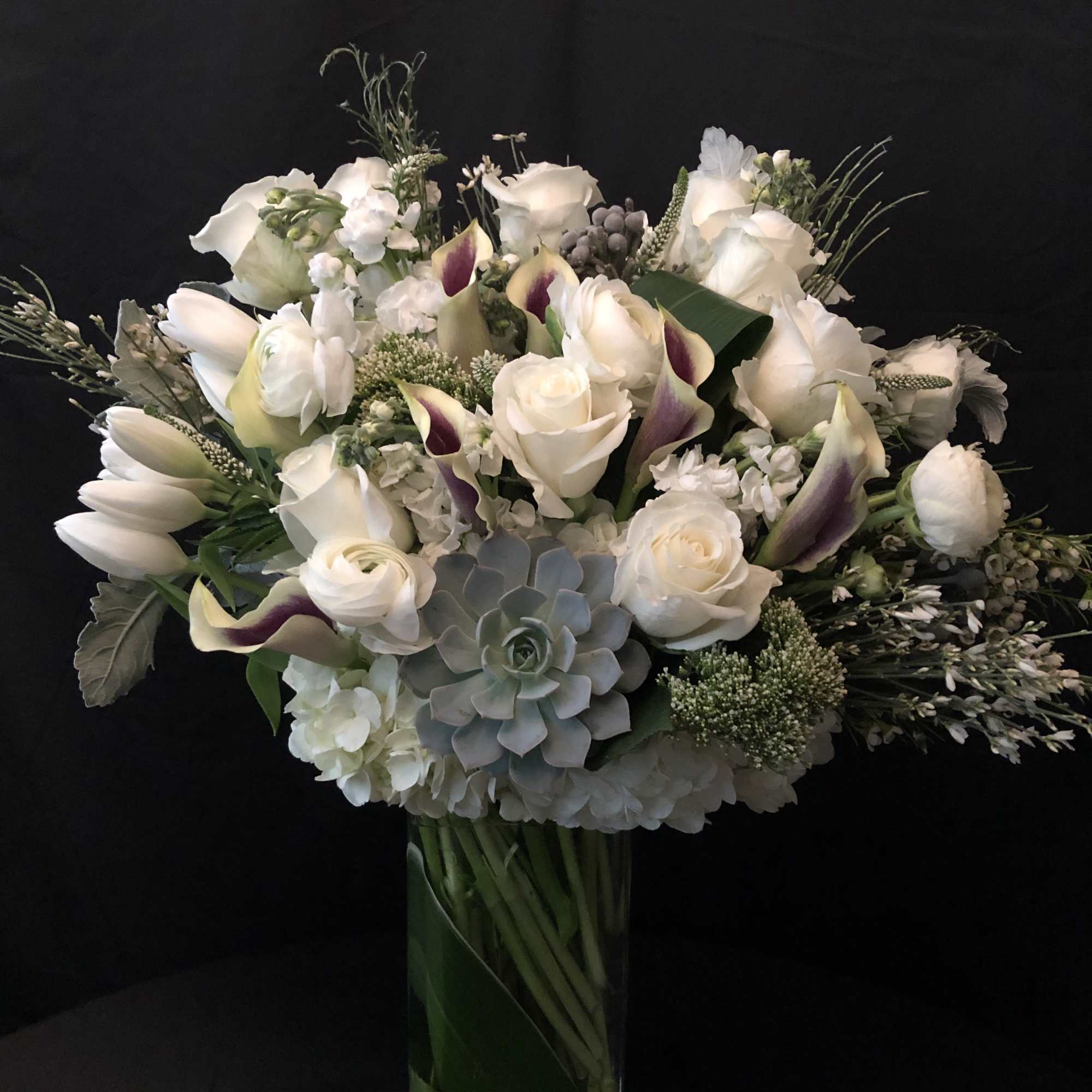 White floral bouquet with calla lilies and roses in a glass vase