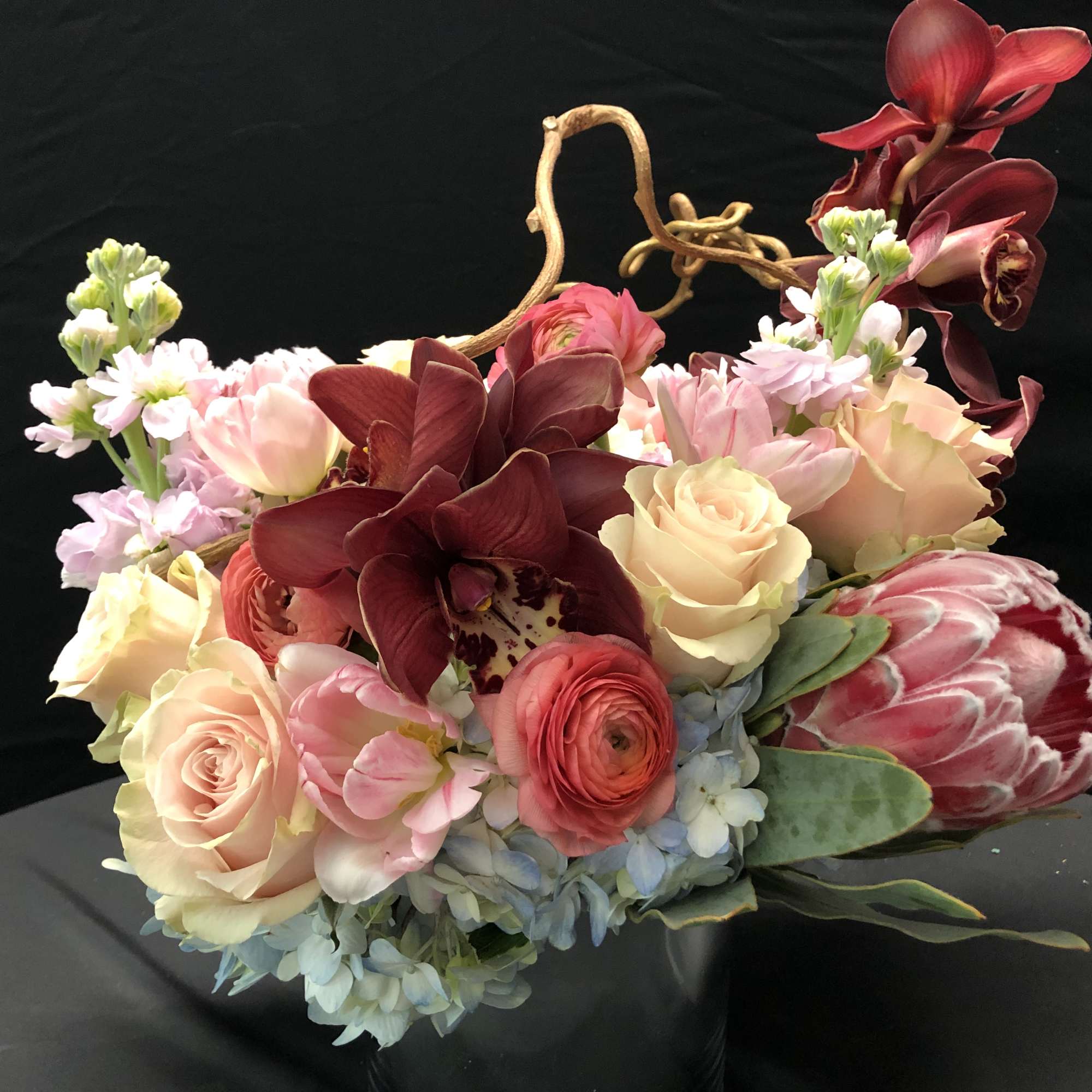 Mixed bouquet with roses, orchids, and protea in pastel and burgundy tones