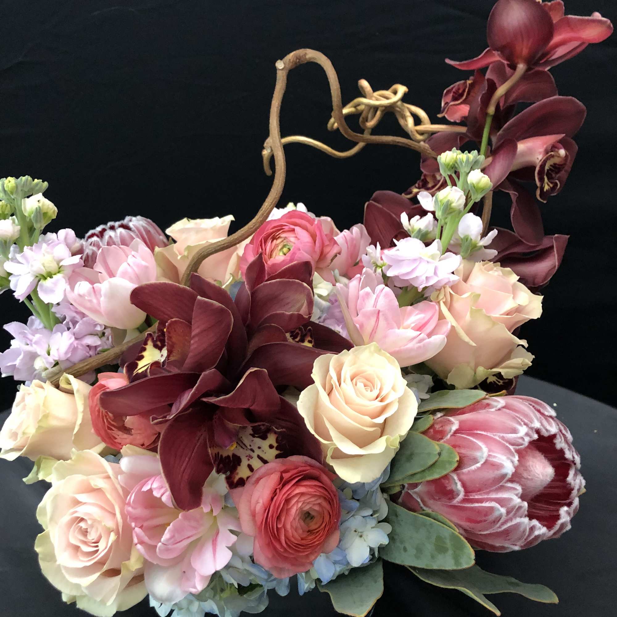 Mixed bouquet with roses, orchids, and pink blooms in a low container