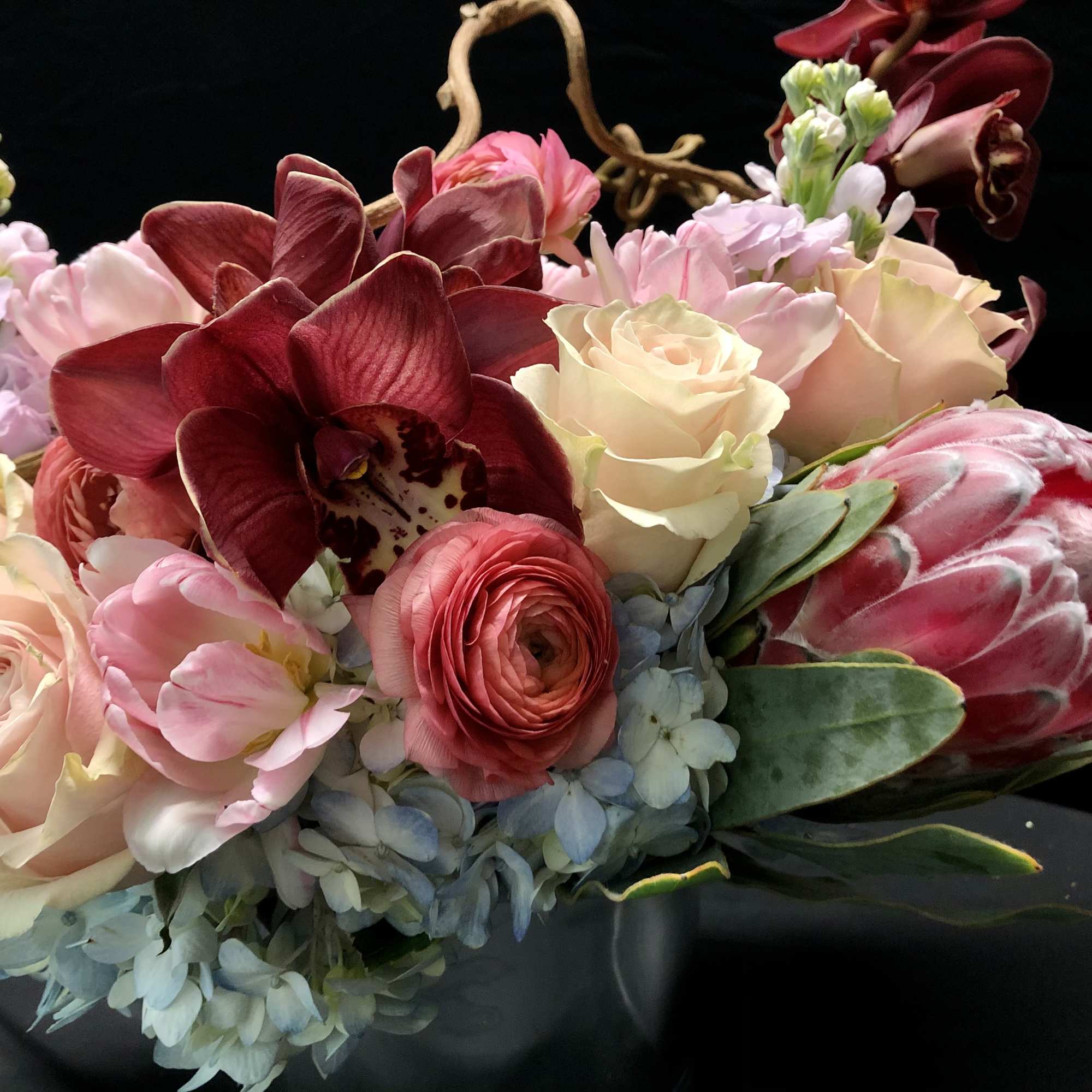 Bouquet of pink and cream flowers with a dark red orchid and protea