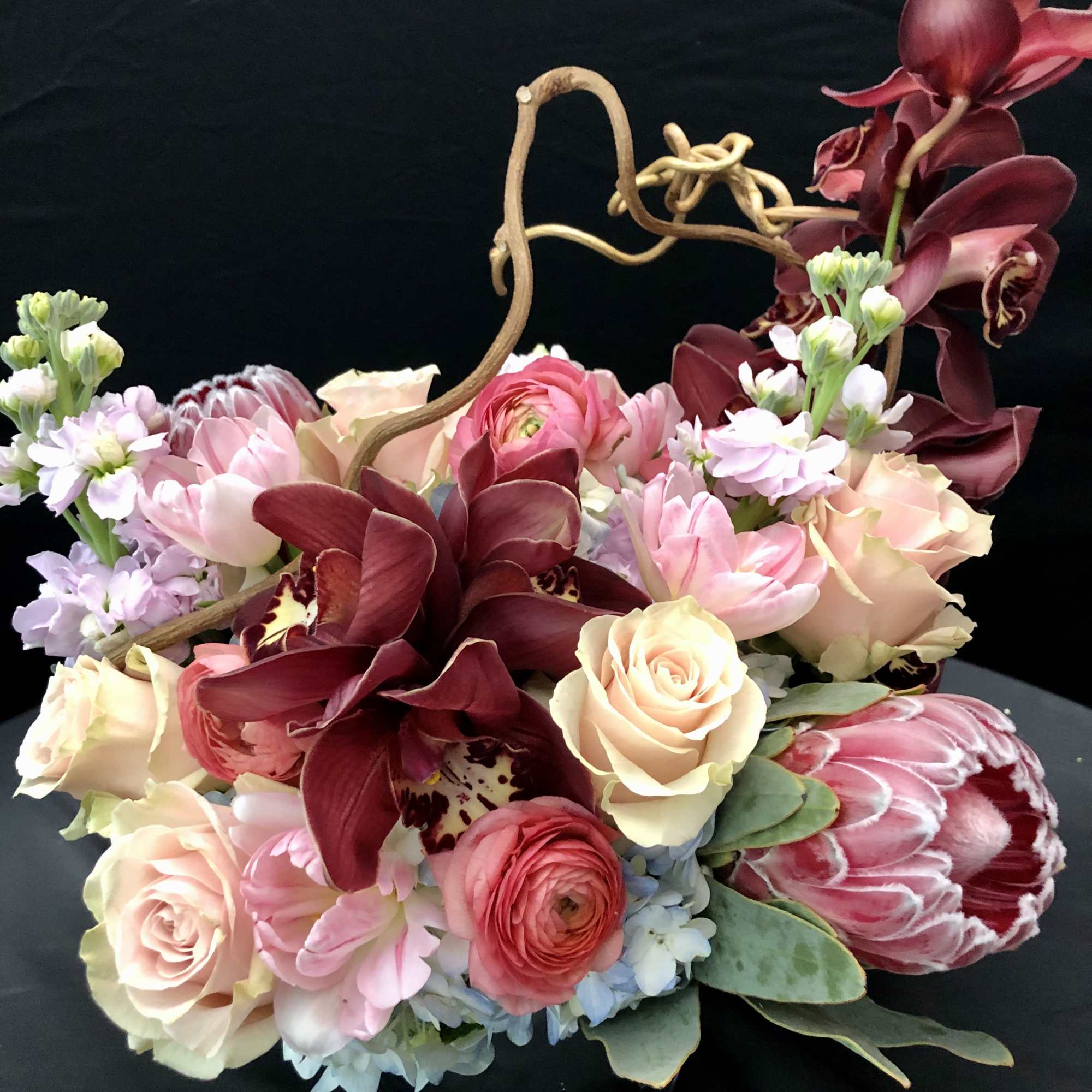 Mixed bouquet with burgundy orchids, pale roses, and pink blooms in a black container