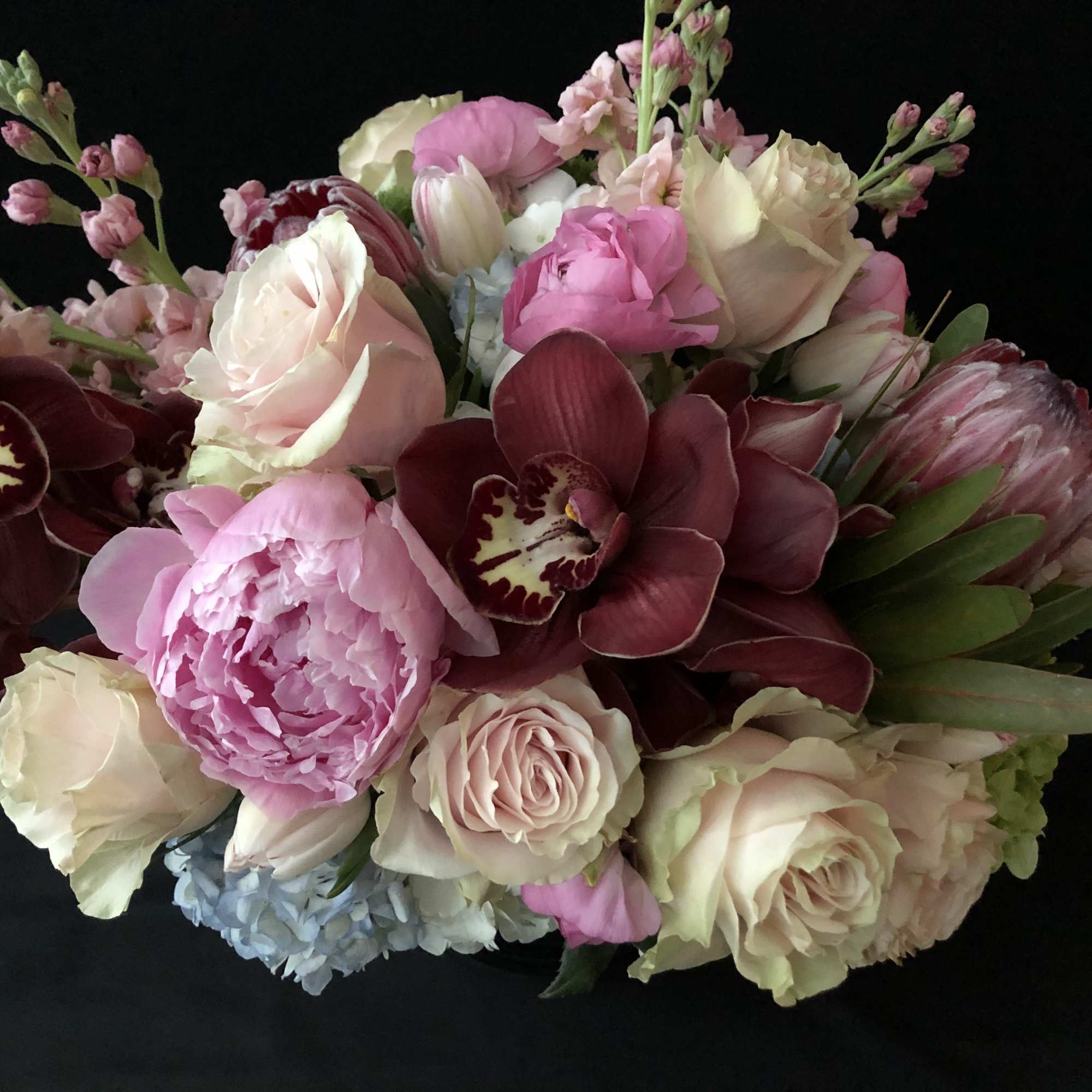 Bouquet of pink and cream roses with burgundy orchids on a black background