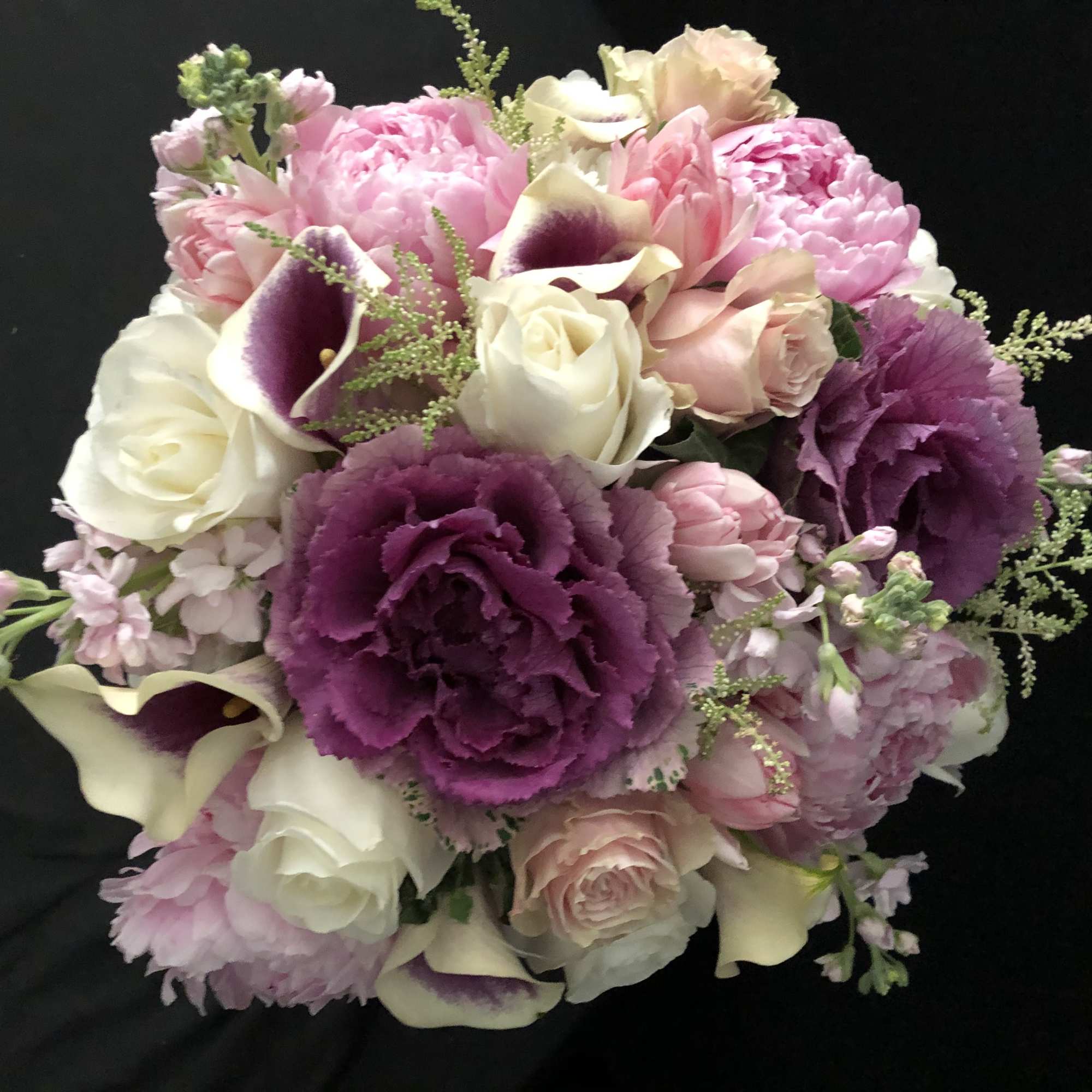 Round bouquet of purple ornamental blooms, pink peonies, and white roses on a black background