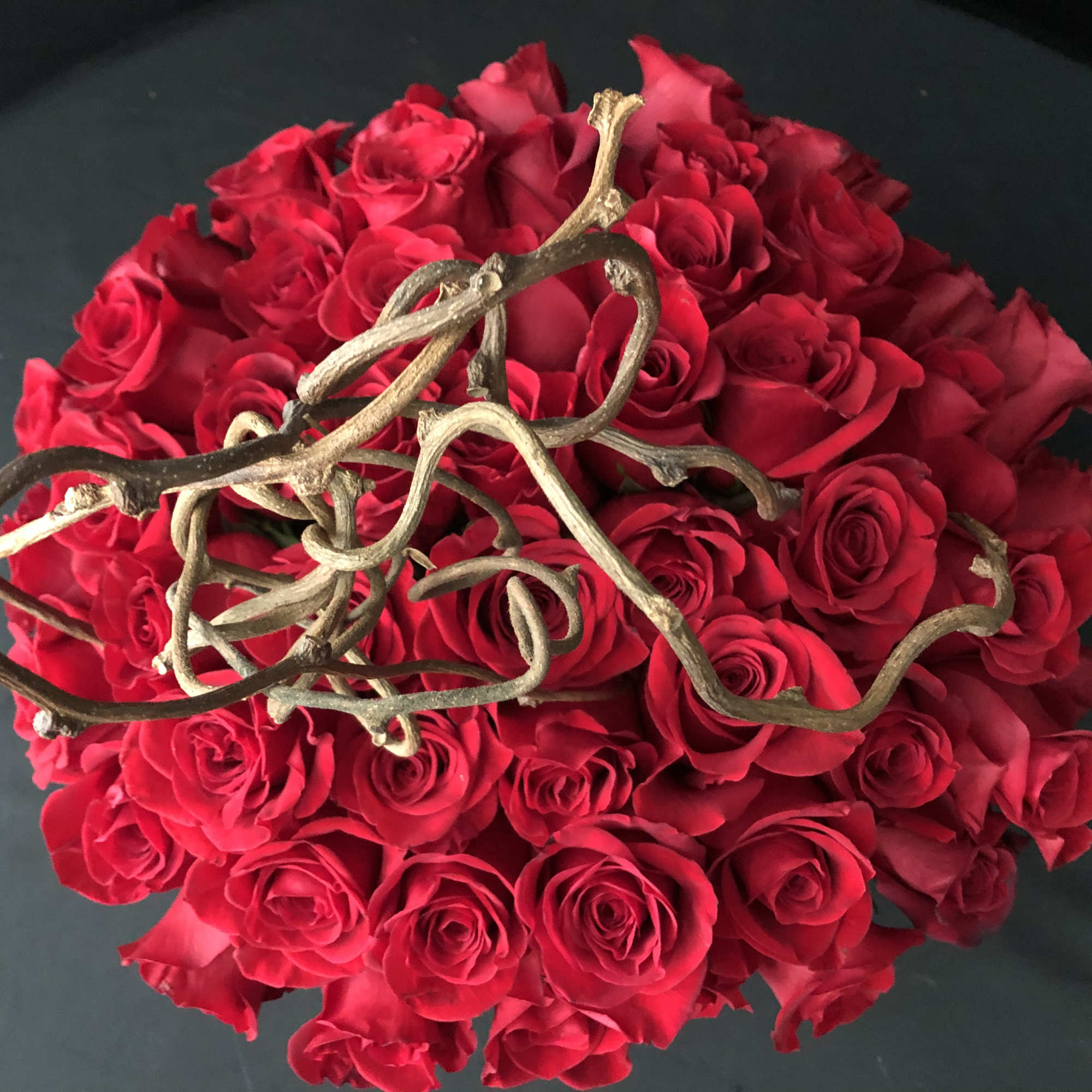 Round bouquet of red roses with twisted gold branches on top