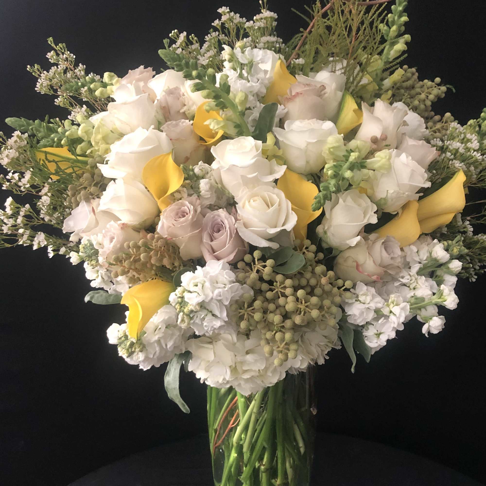 Large bouquet of white roses, yellow calla lilies, and pale pink blooms in a glass vase