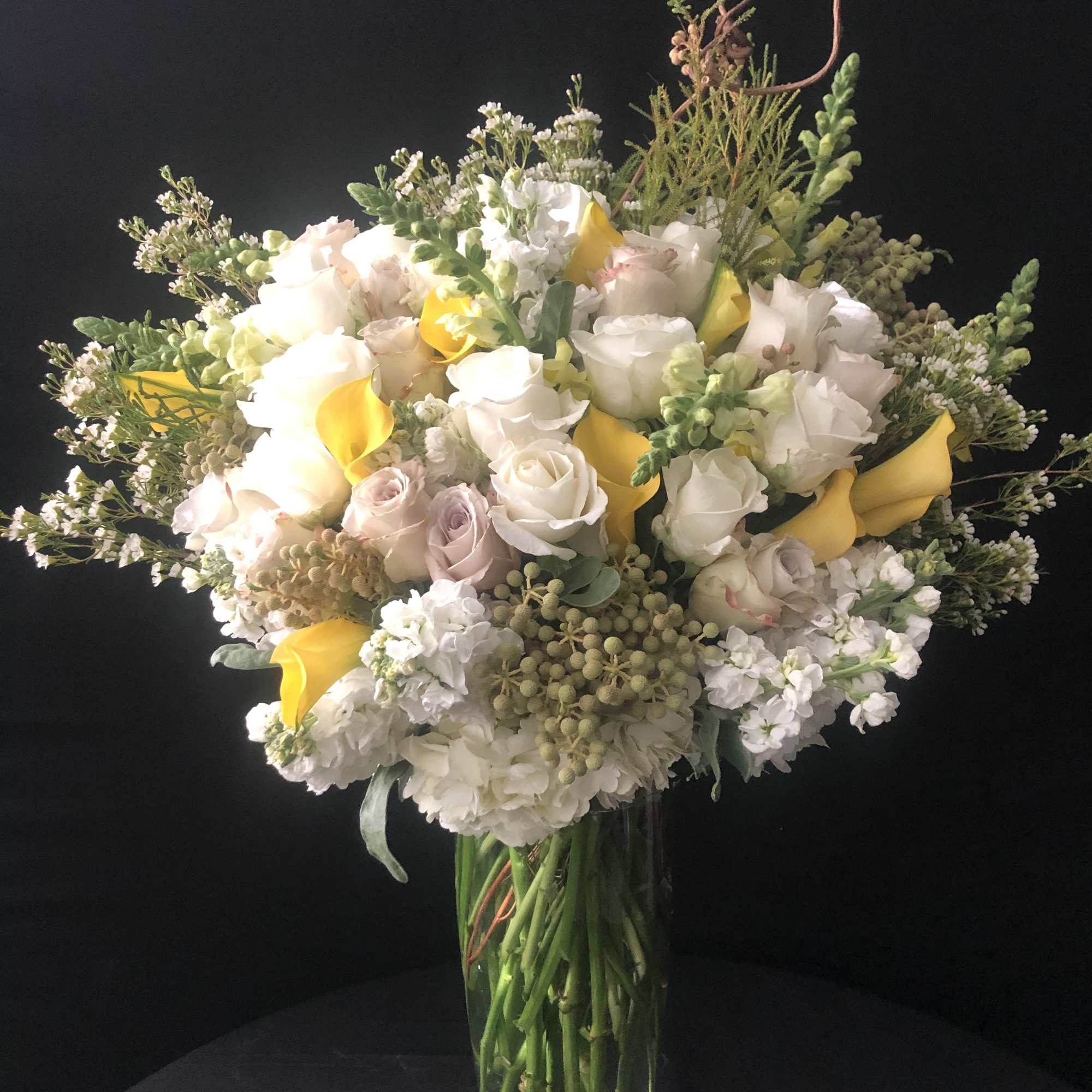 White and pale pink roses with yellow calla lilies in a glass vase