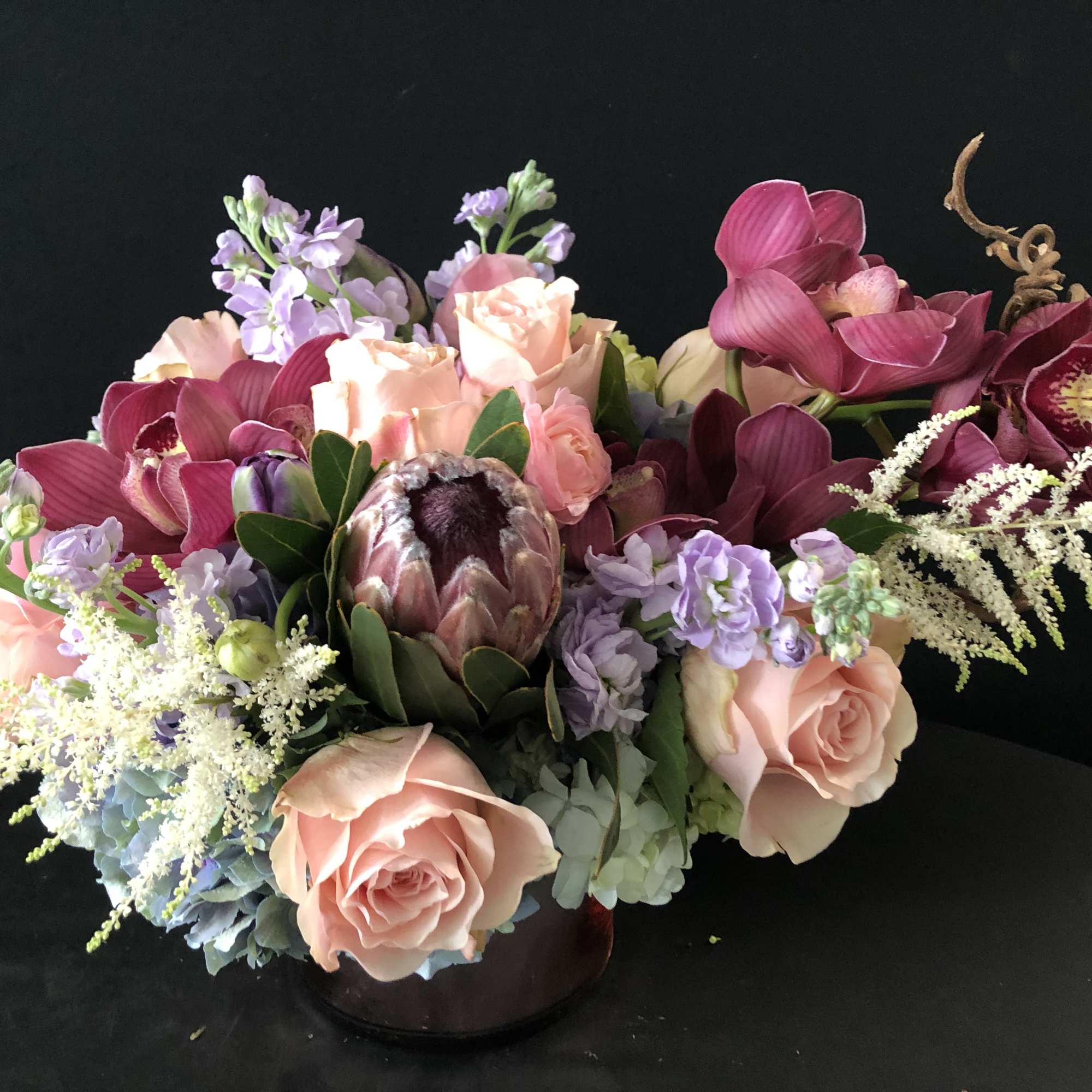 Mixed bouquet of pink roses, purple orchids, and a protea in a low vase