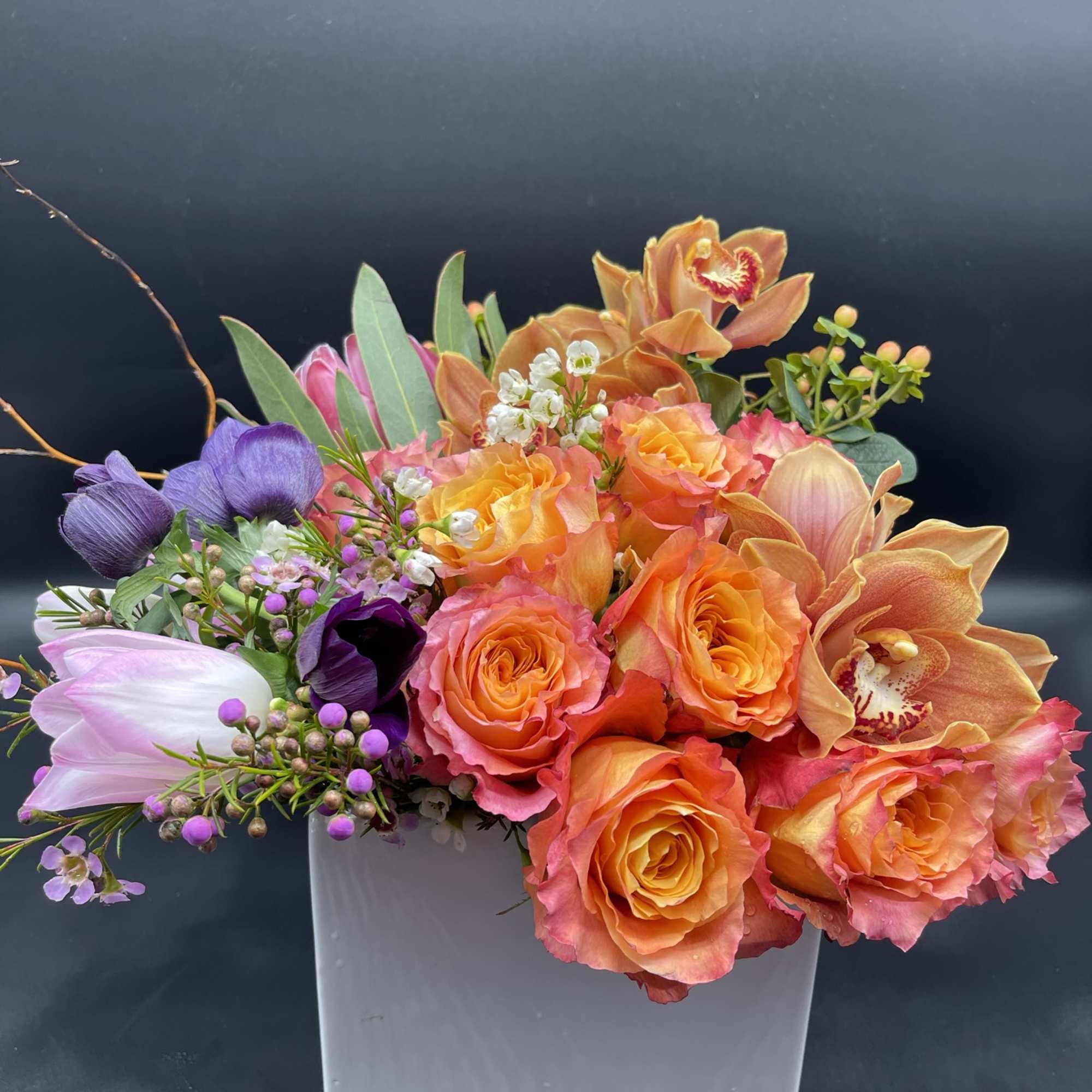 Colorful bouquet of roses, orchids, and tulips in a white square vase