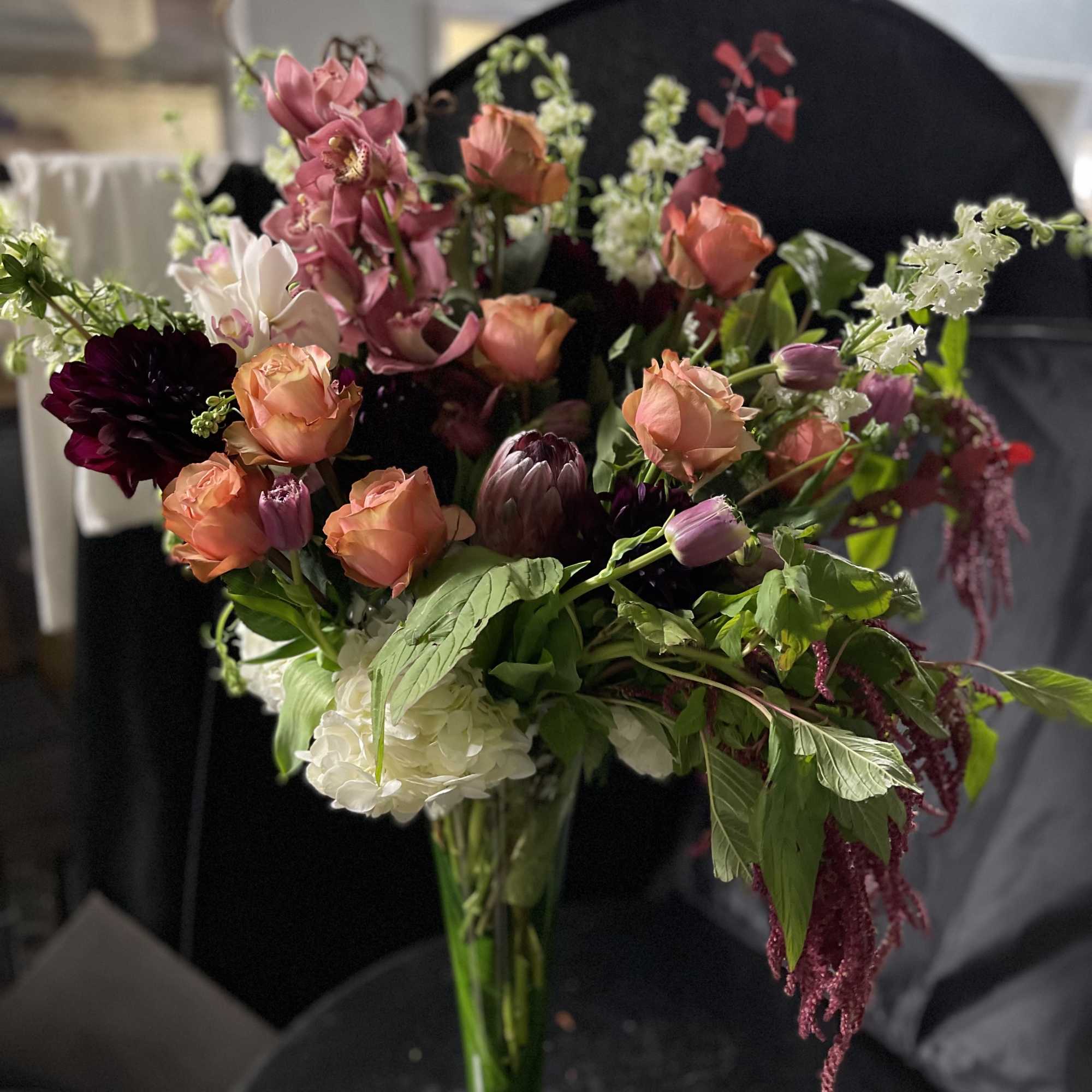 Mixed bouquet of peach, pink, white, and dark burgundy flowers in a glass vase