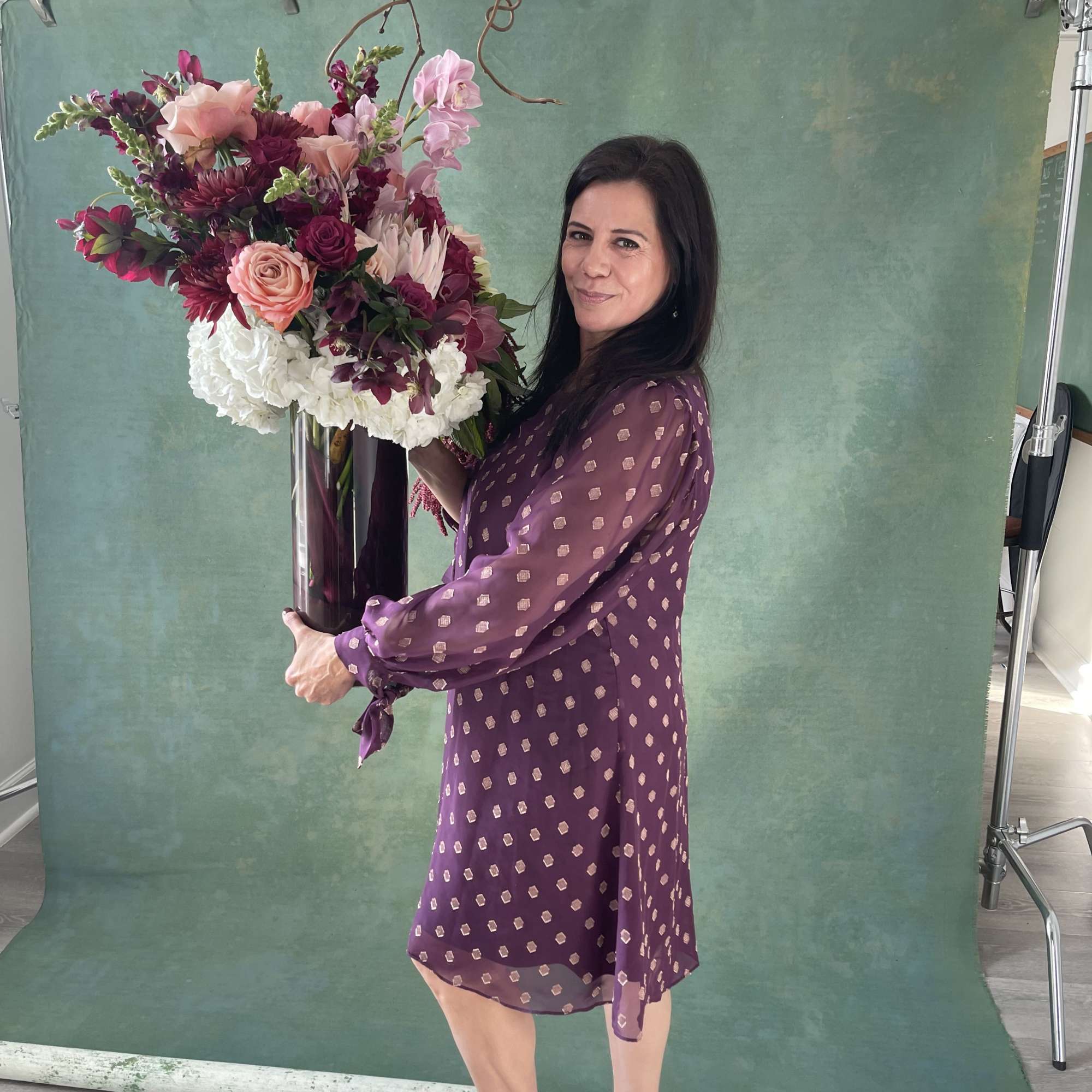 Woman holding a tall floral arrangement in a vase