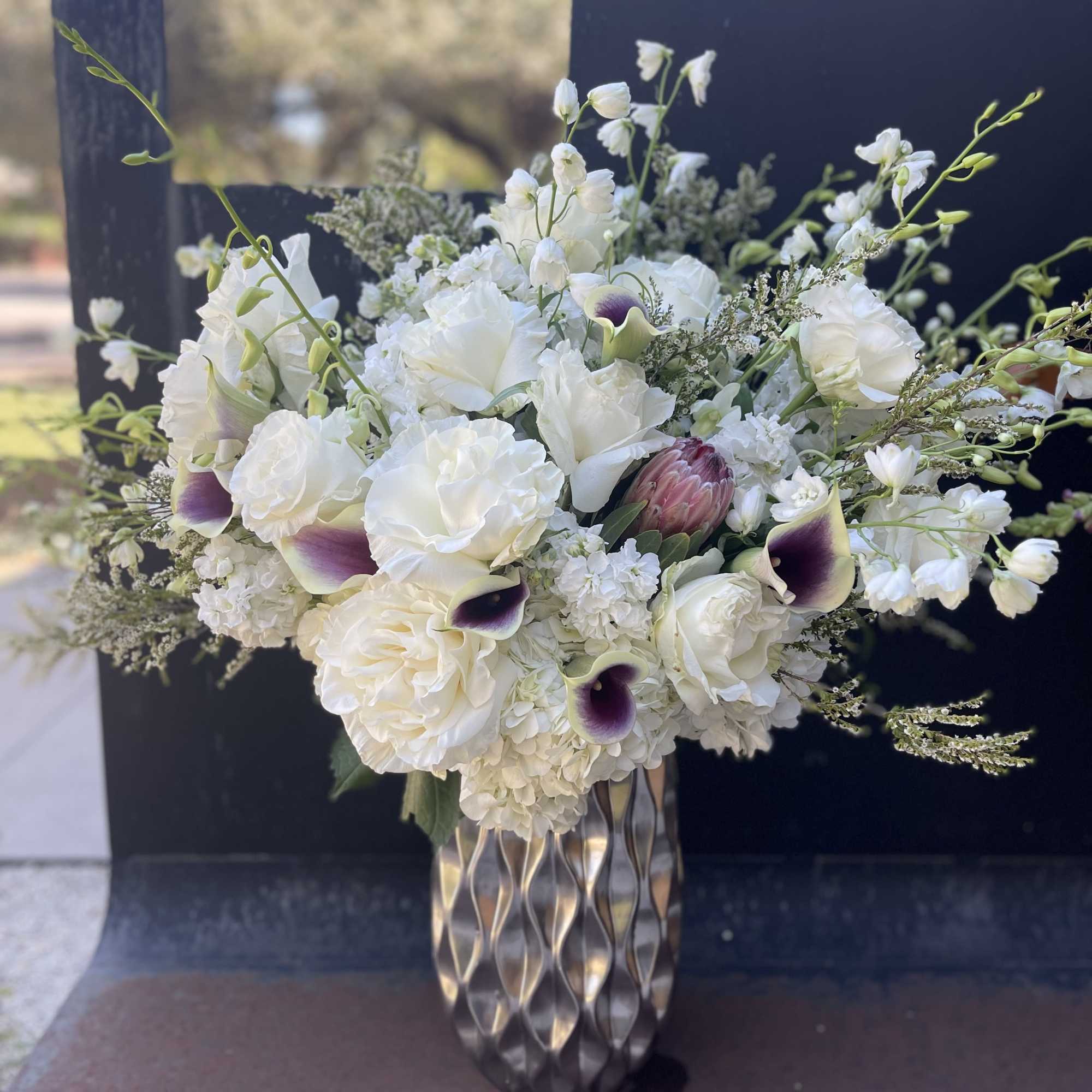 White floral arrangement with calla lilies and roses in a silver vase