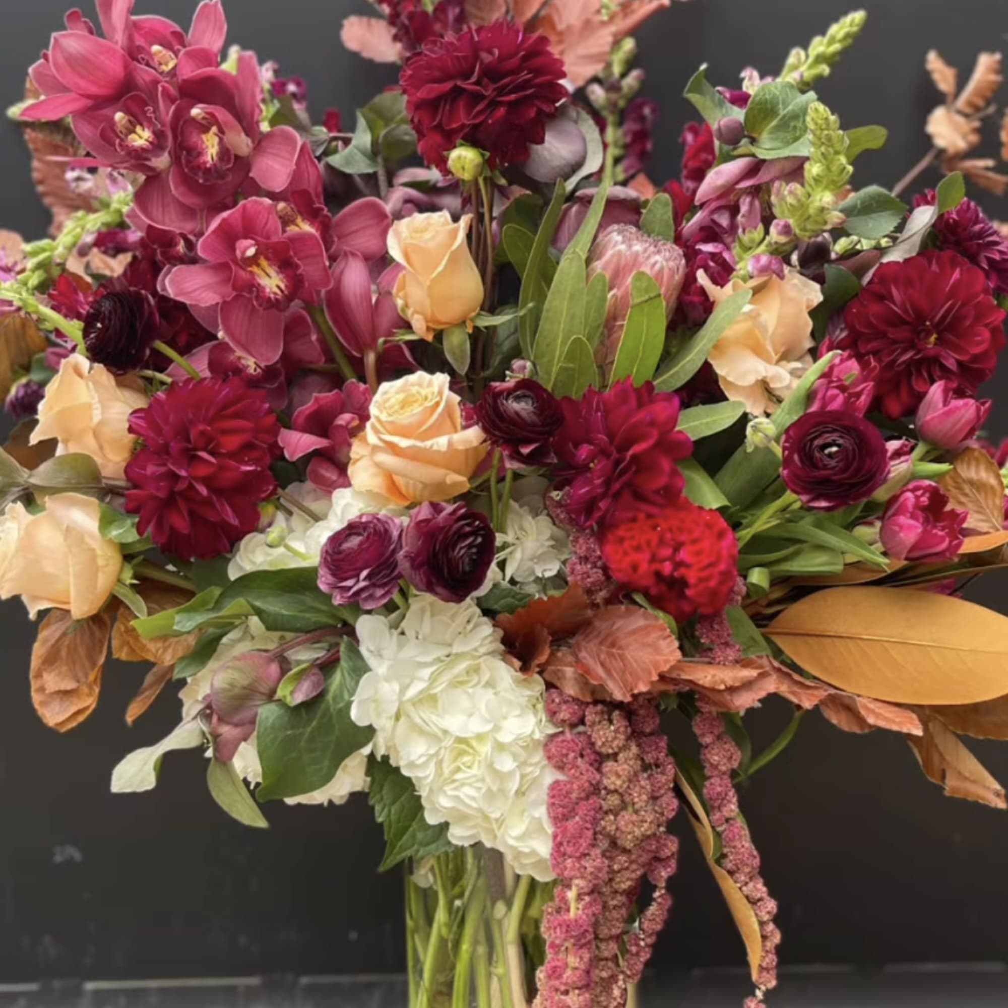 Large bouquet of burgundy, peach, and white flowers in a glass vase