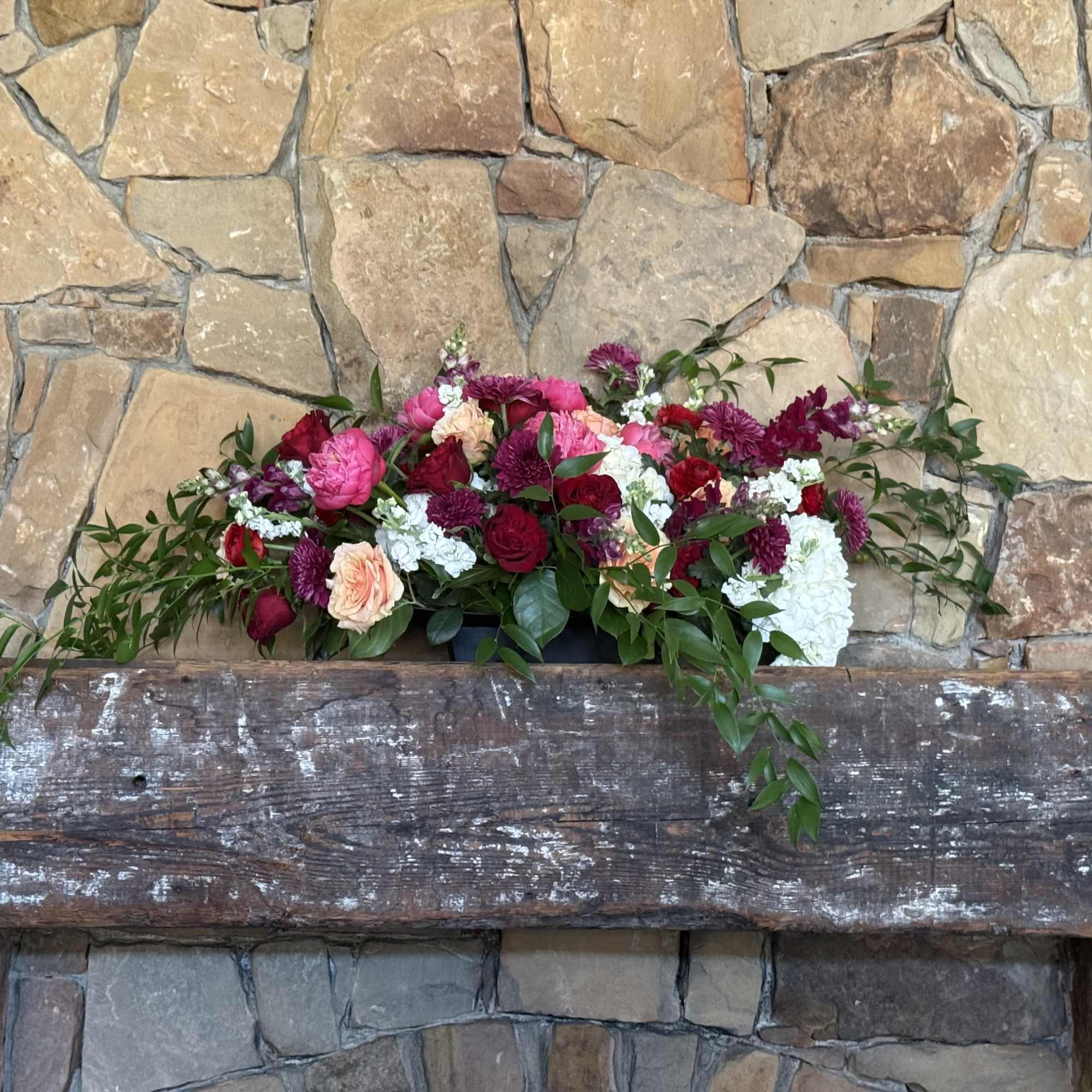 Long floral arrangement with pink, red, white, and peach blooms on a rustic beam
