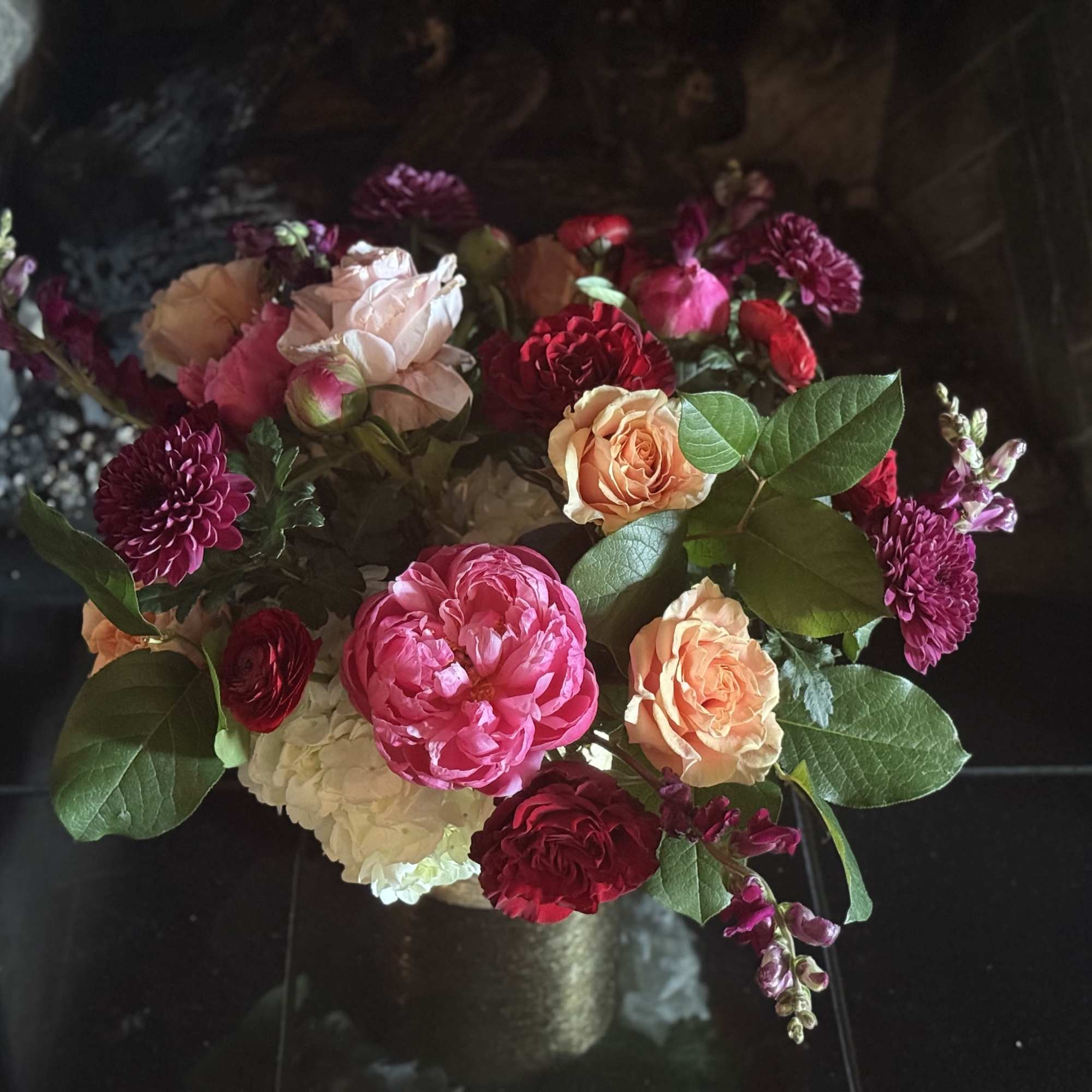 Mixed bouquet of pink, peach, and burgundy flowers in a dark vase