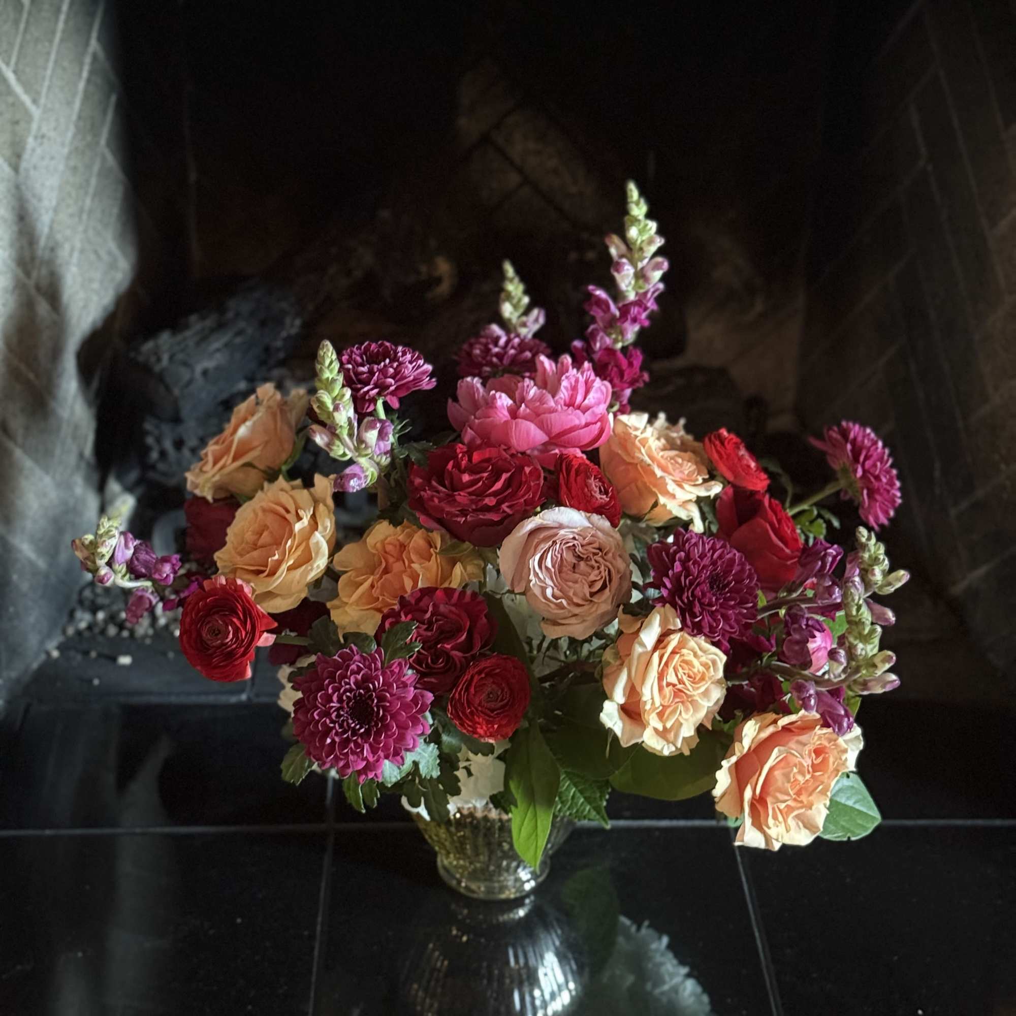 Mixed bouquet of peach, pink, and red flowers in a glass vase