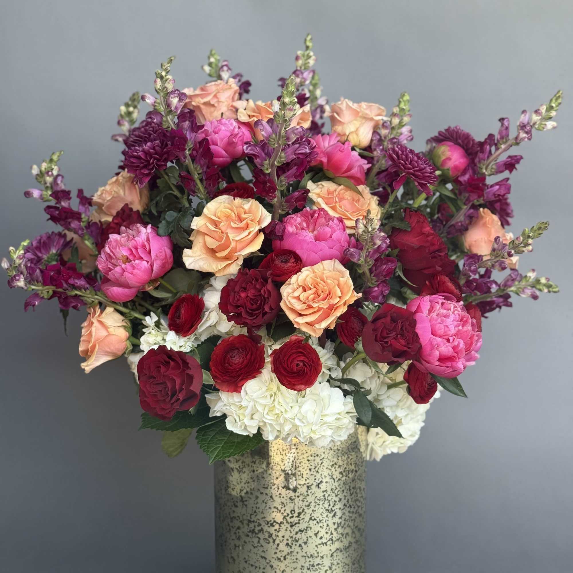 Mixed pink, peach, red, and white flowers in a gold vase