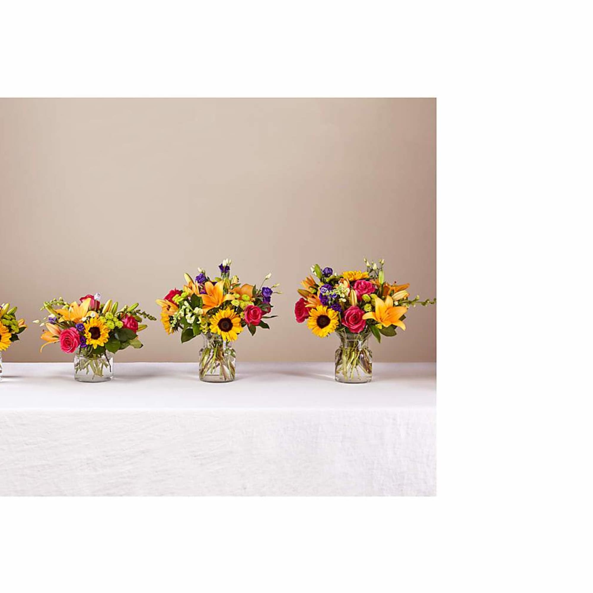 Four small mixed flower arrangements in clear glass vases on a table