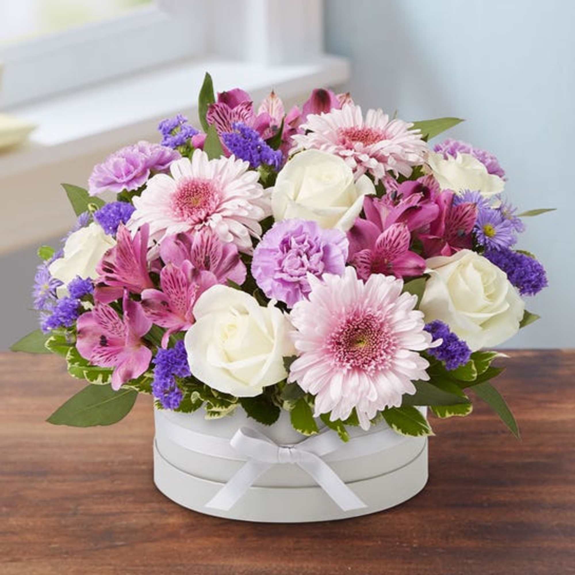 Pink and white mixed flower arrangement in a round white box
