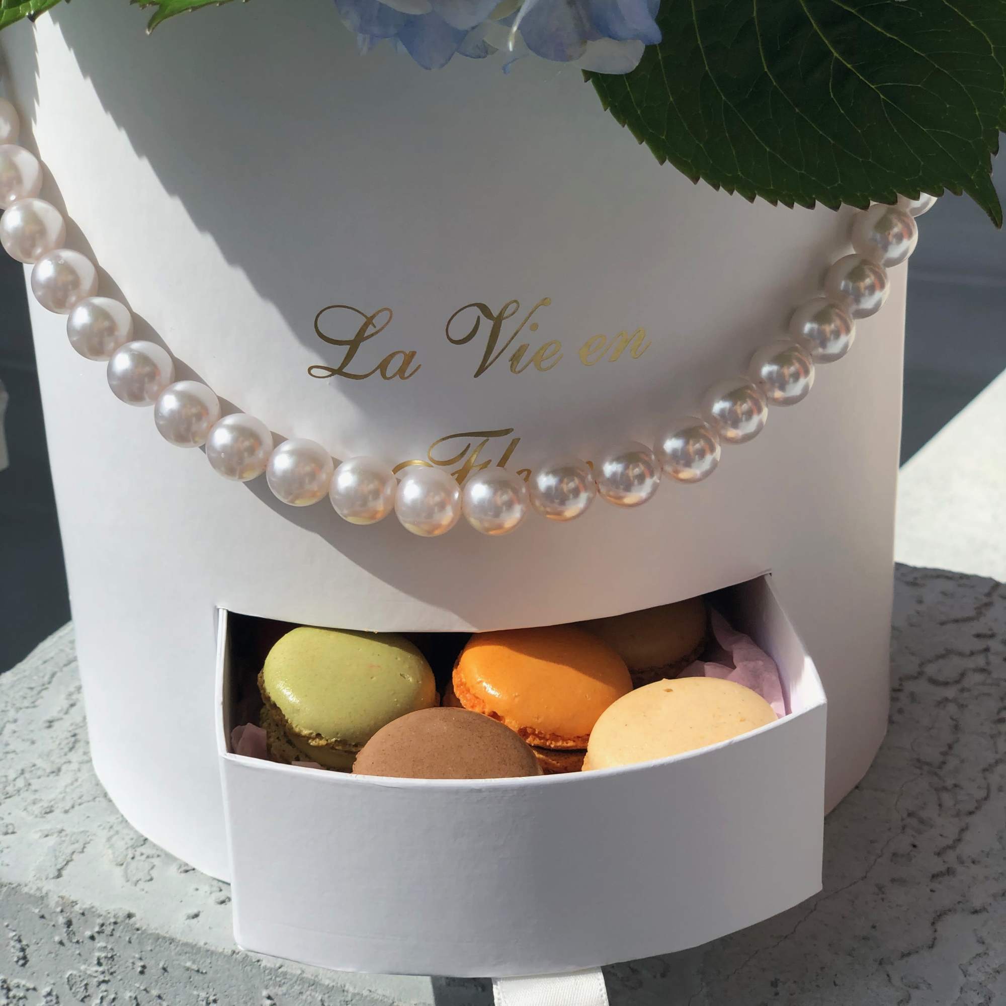 White gift box with blue hydrangeas and a drawer of colorful macarons