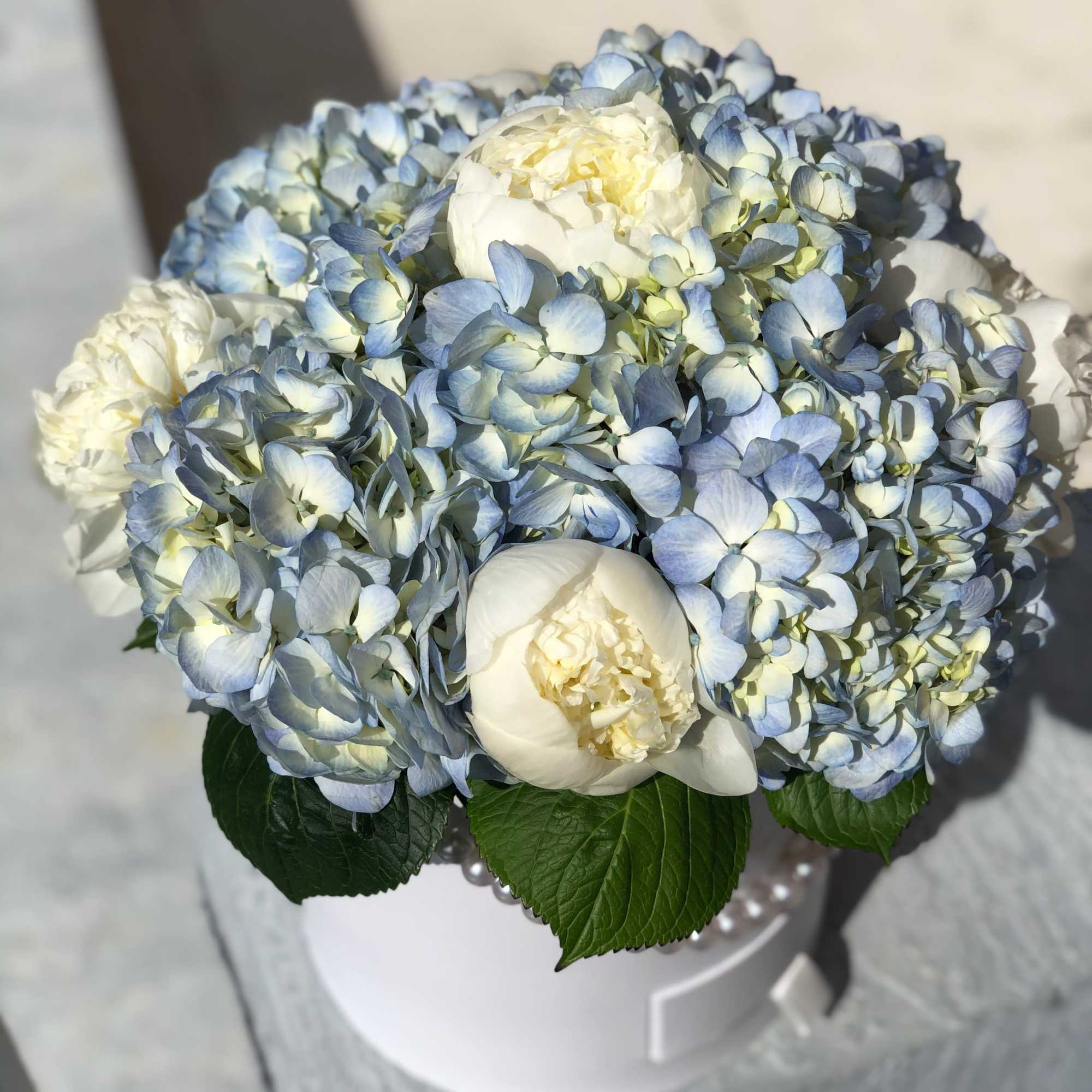 Blue hydrangea and white peony bouquet in a white hat box