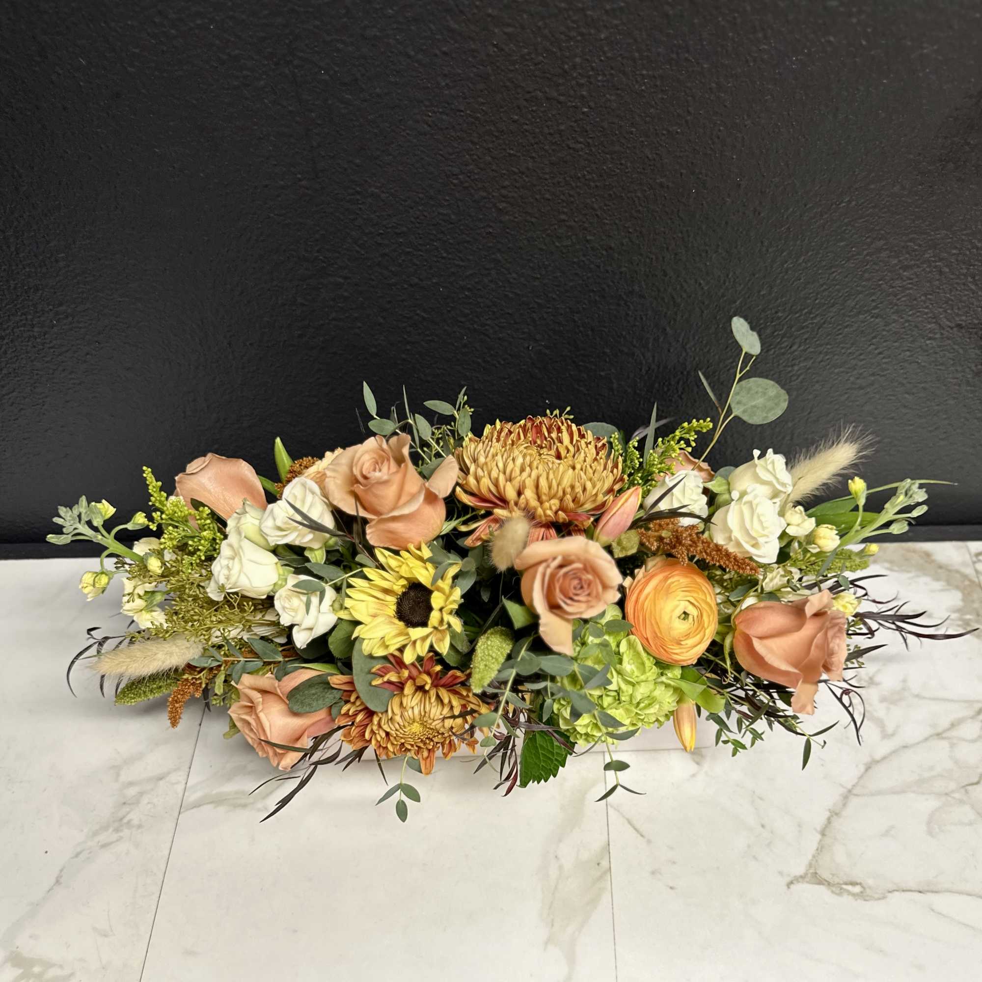 Low floral arrangement with peach roses, white blooms, and yellow flowers