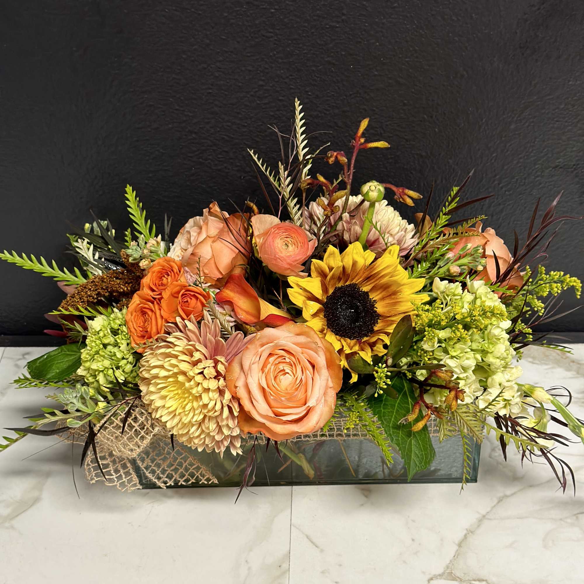 Mixed floral arrangement with peach roses and a sunflower in a low rectangular vase