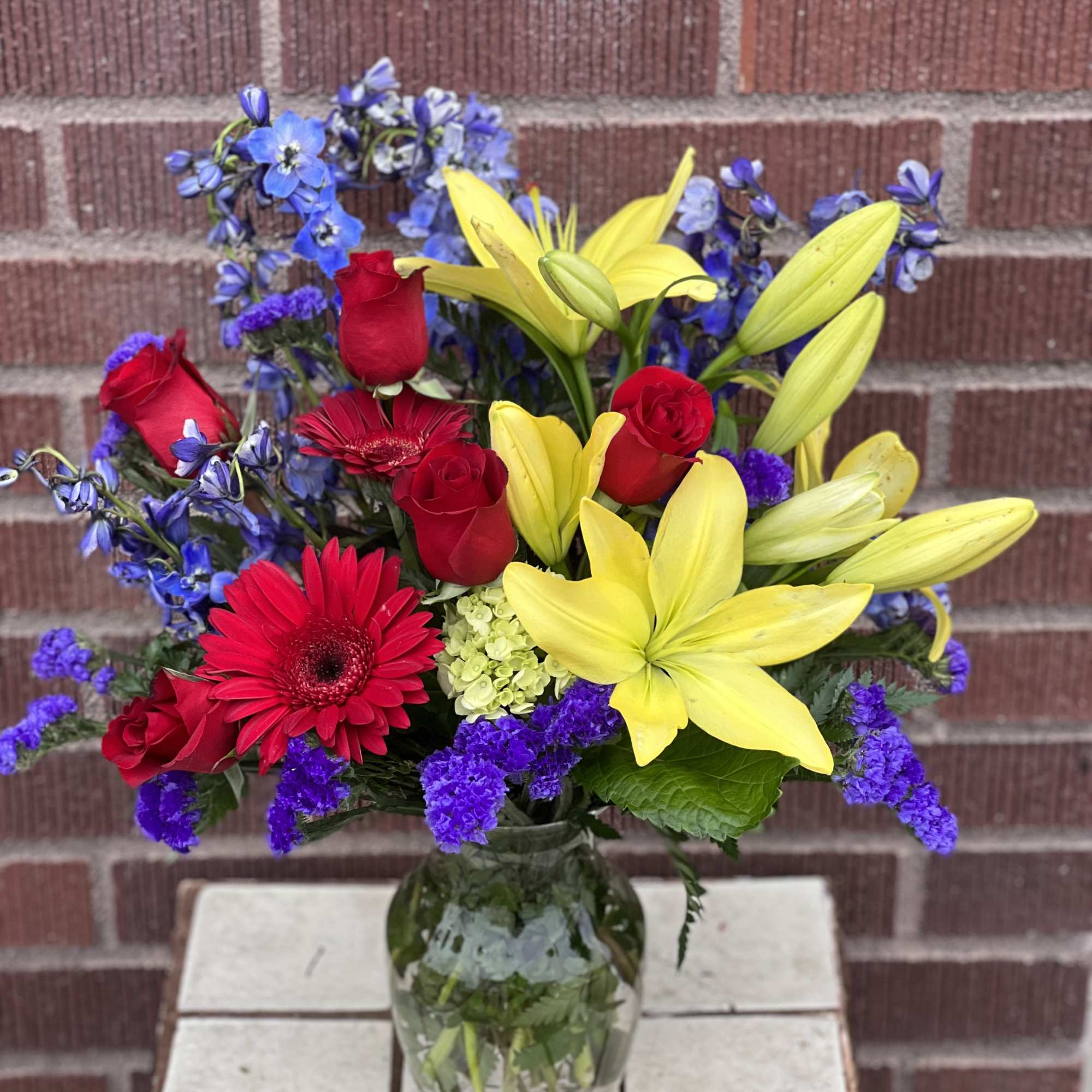 Bouquet of red roses, yellow lilies, and blue flowers in a glass vase
