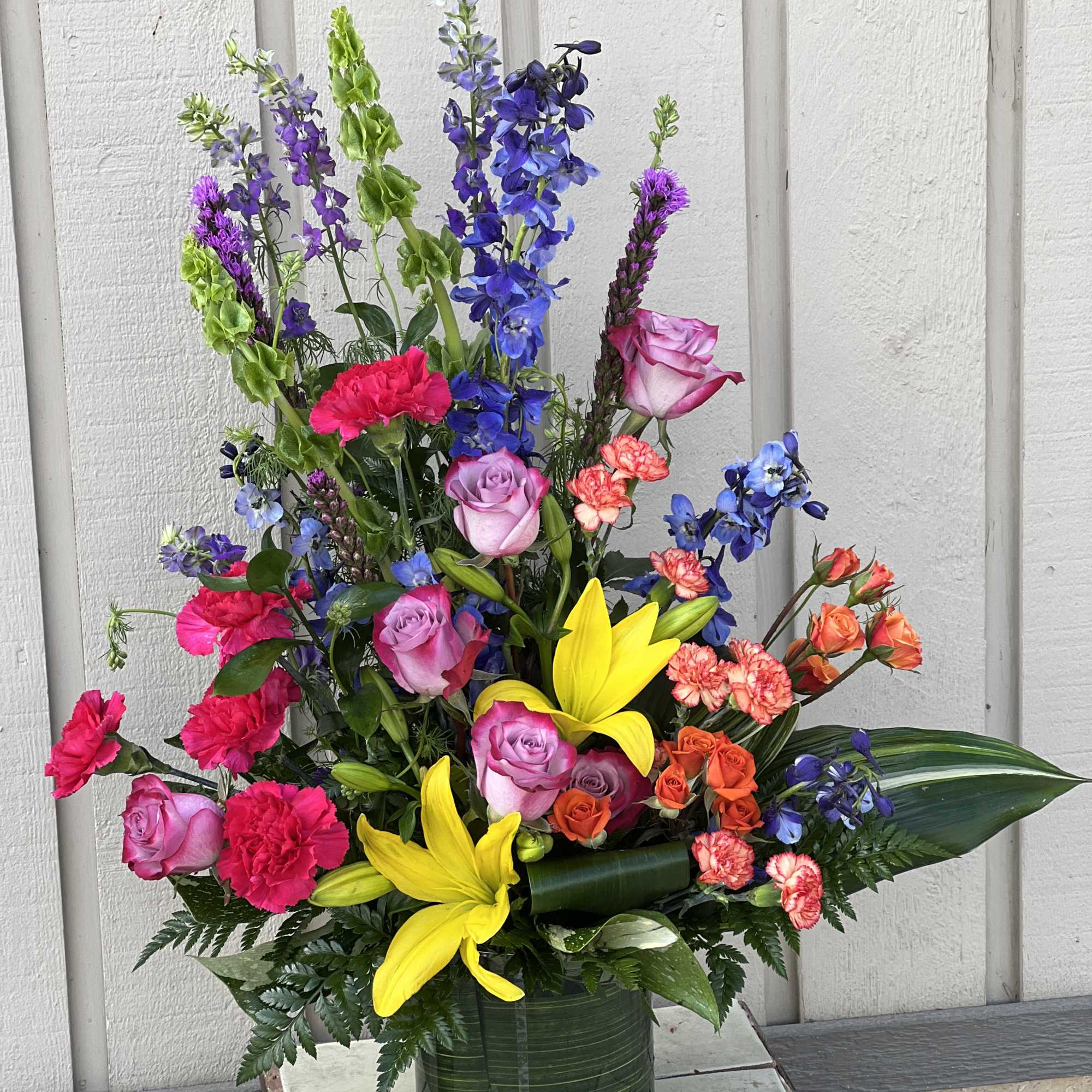 Colorful mixed bouquet in a green vase with lilies, roses, and carnations