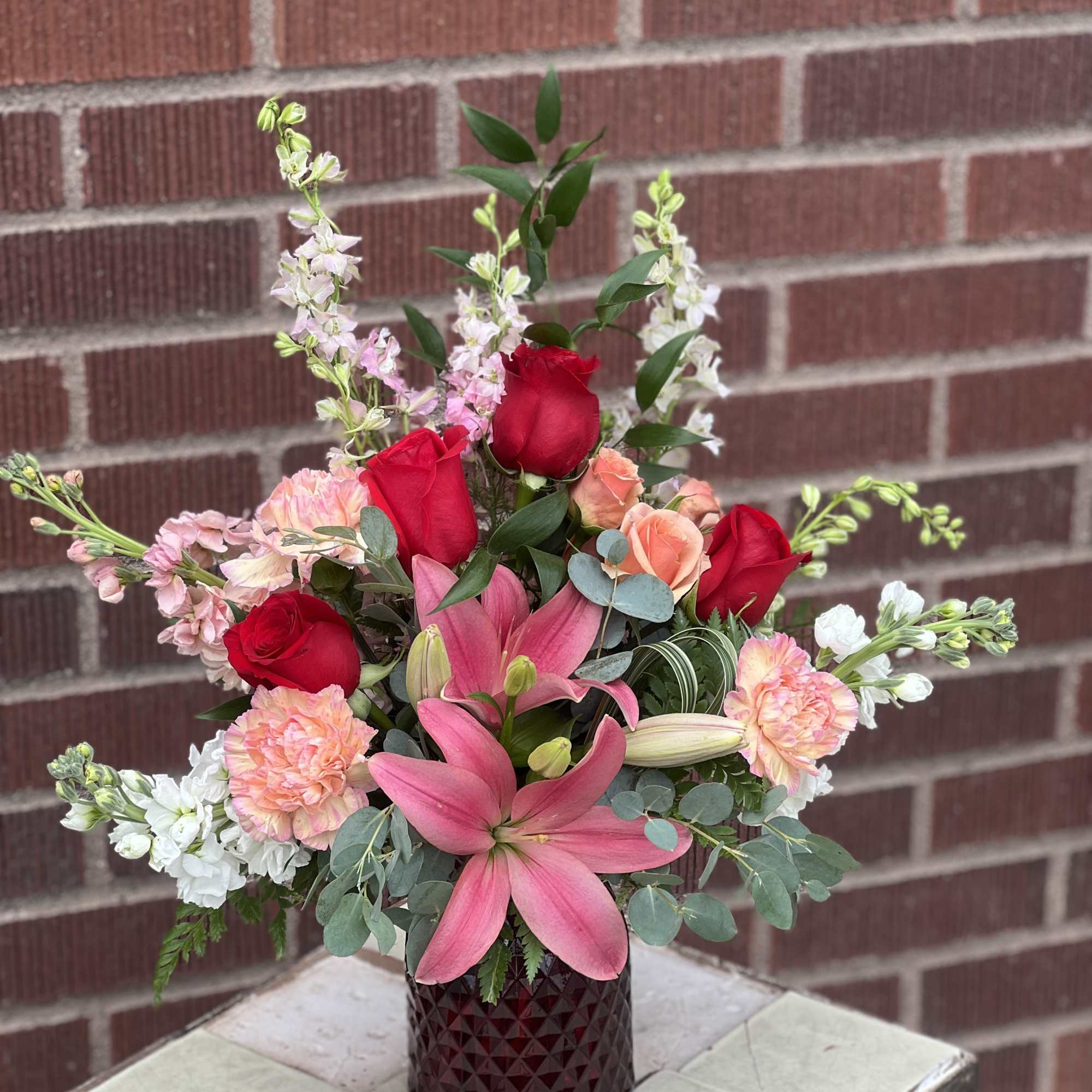 Bouquet of red roses, pink lilies, and peach carnations in a dark vase
