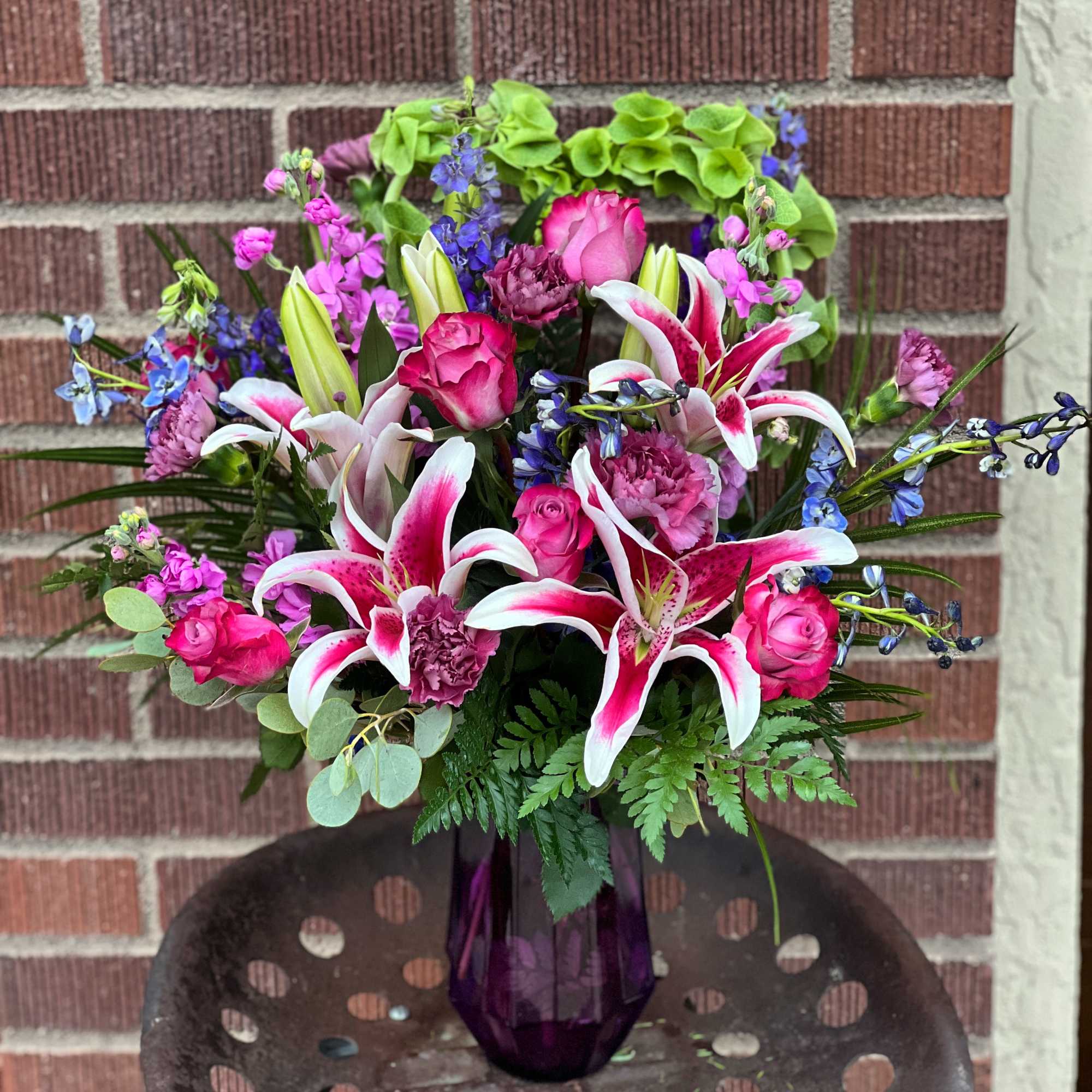 Bouquet of pink lilies, roses, and purple flowers in a purple vase
