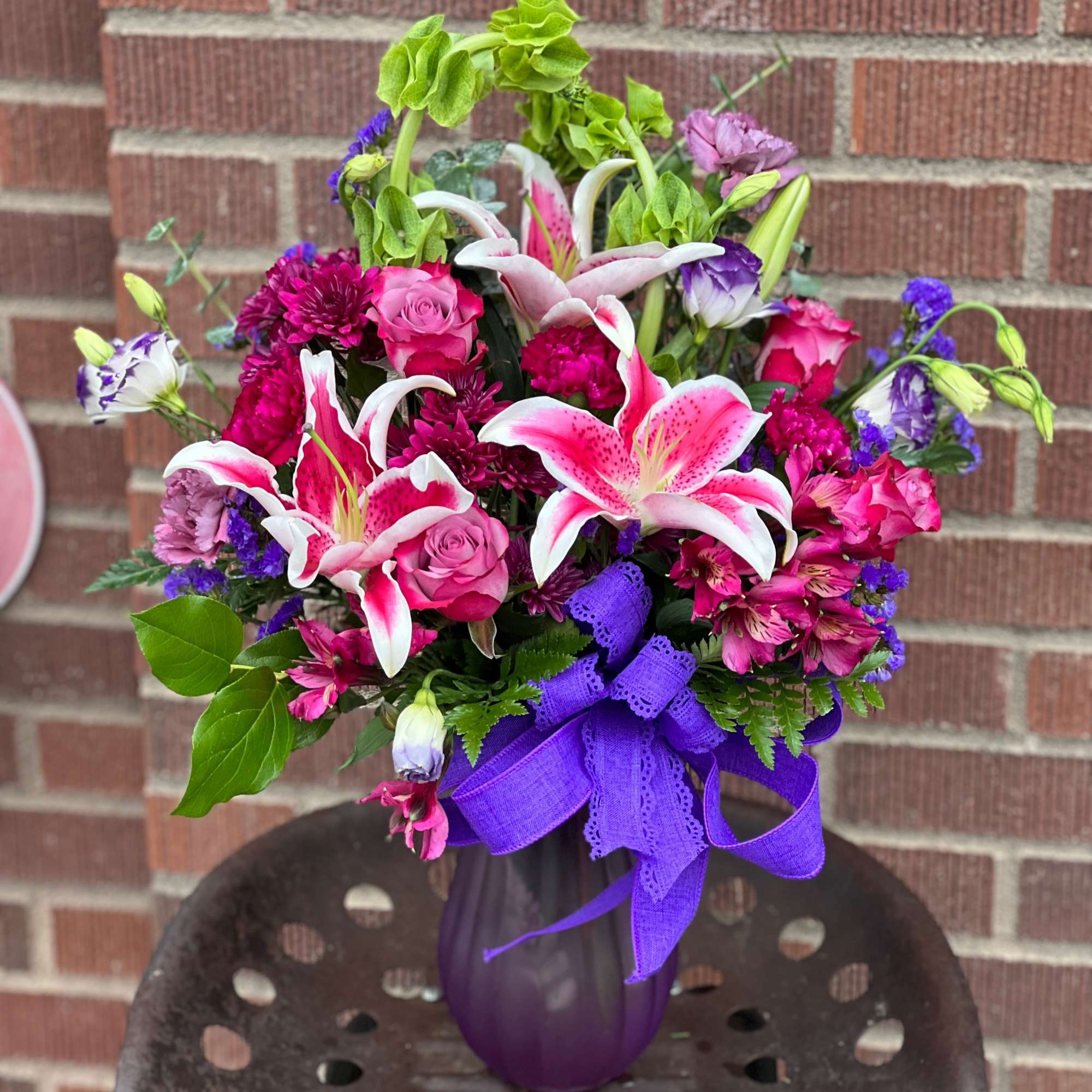 Bouquet of pink lilies, roses, and purple flowers in a purple vase