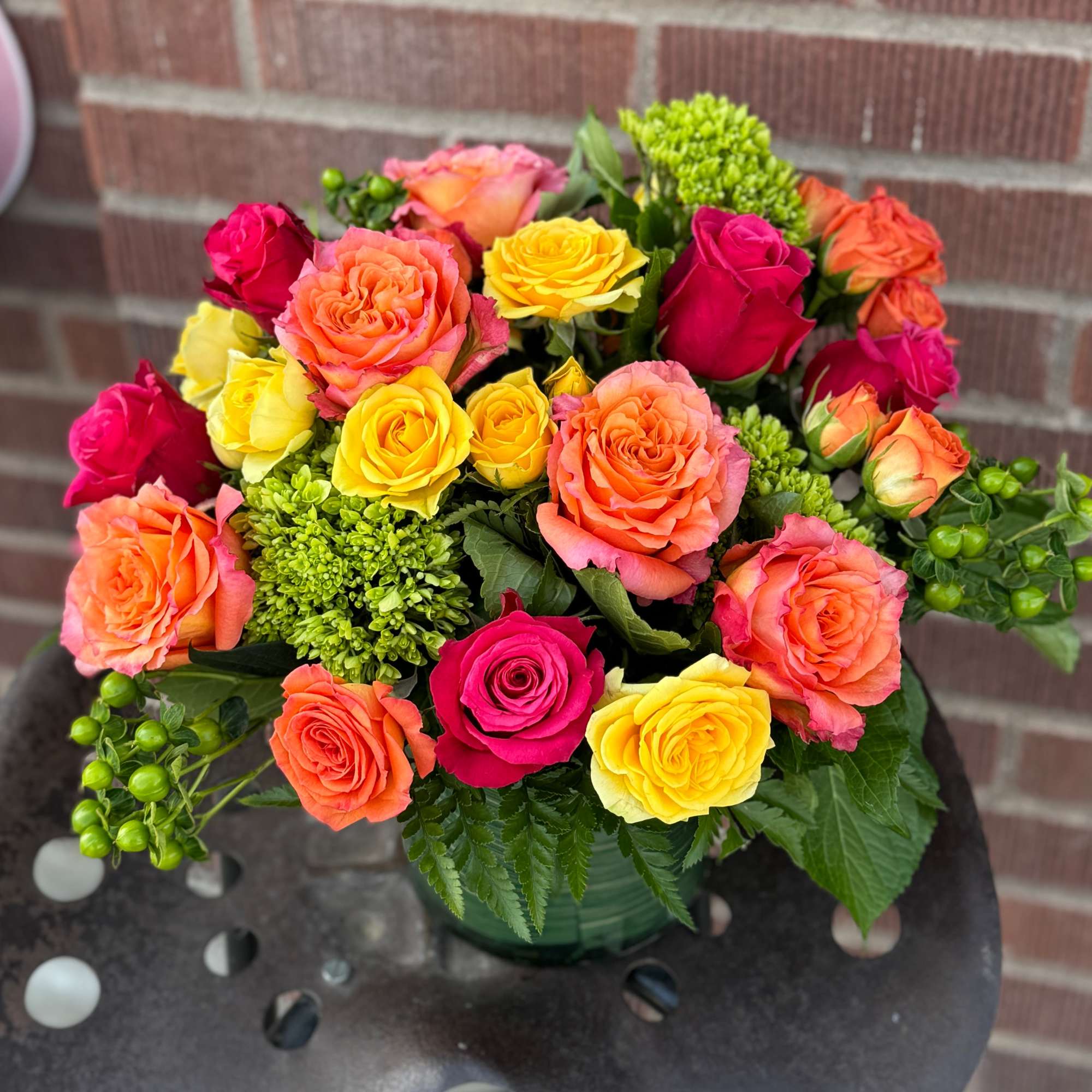 Mixed bouquet of pink, orange, and yellow roses in a green vase