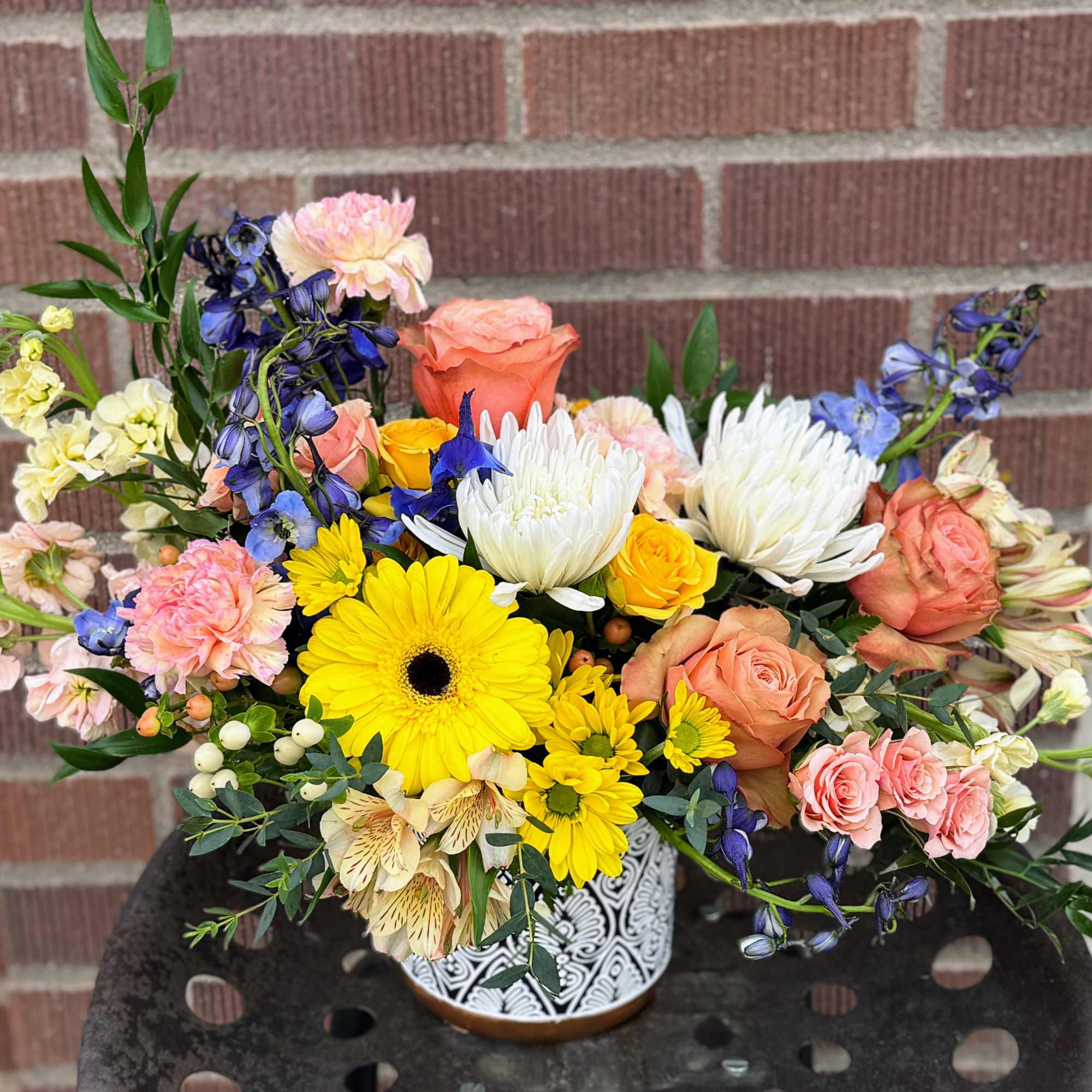 Mixed bouquet in a patterned vase with yellow, pink, white, and blue flowers