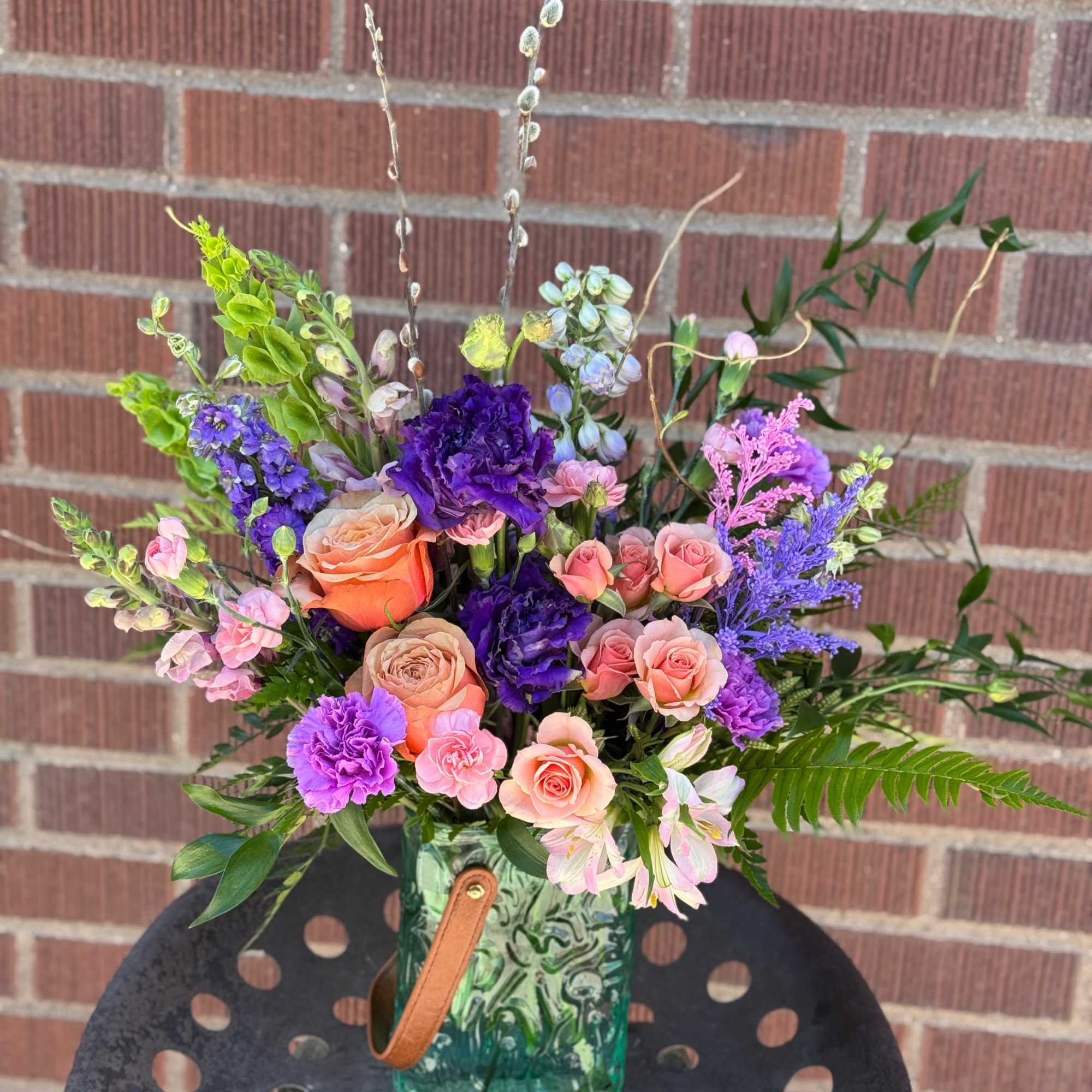 Peach and blush roses meet vivid purple carnations in a lively, garden-style