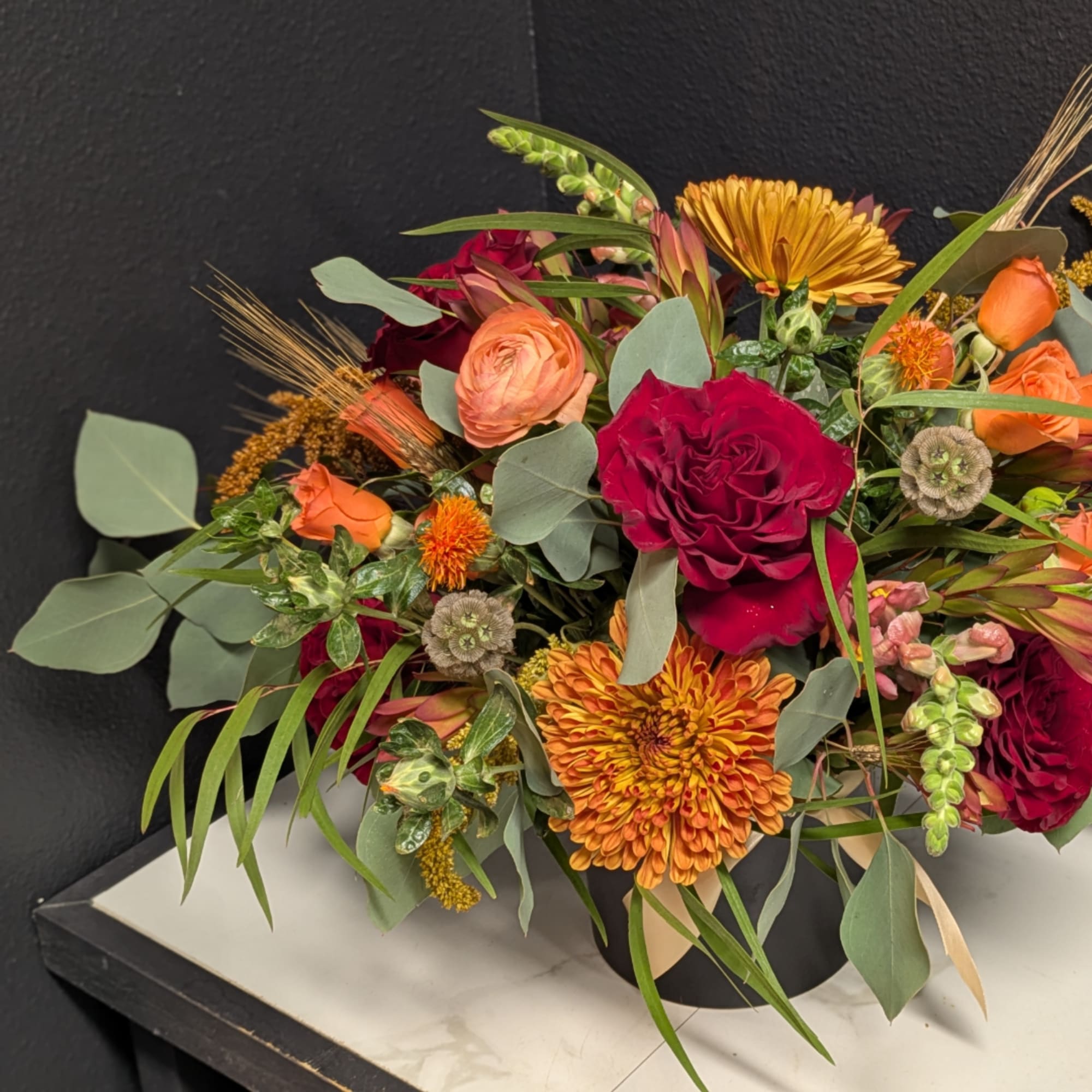 Mixed bouquet with red, orange, and peach flowers in a black container
