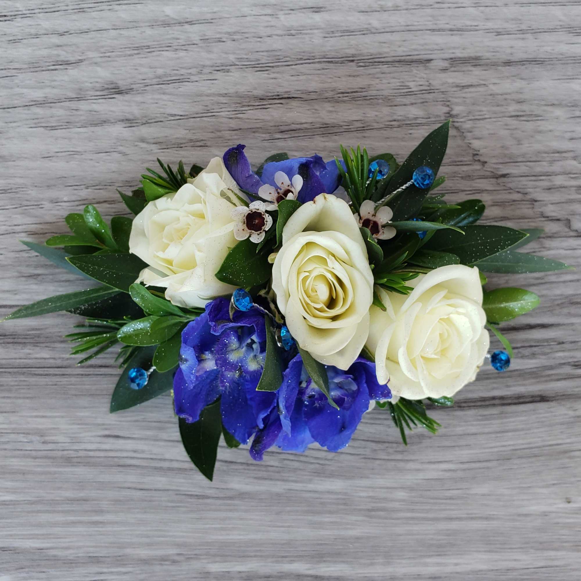 White roses and blue flowers in a small arrangement with greenery
