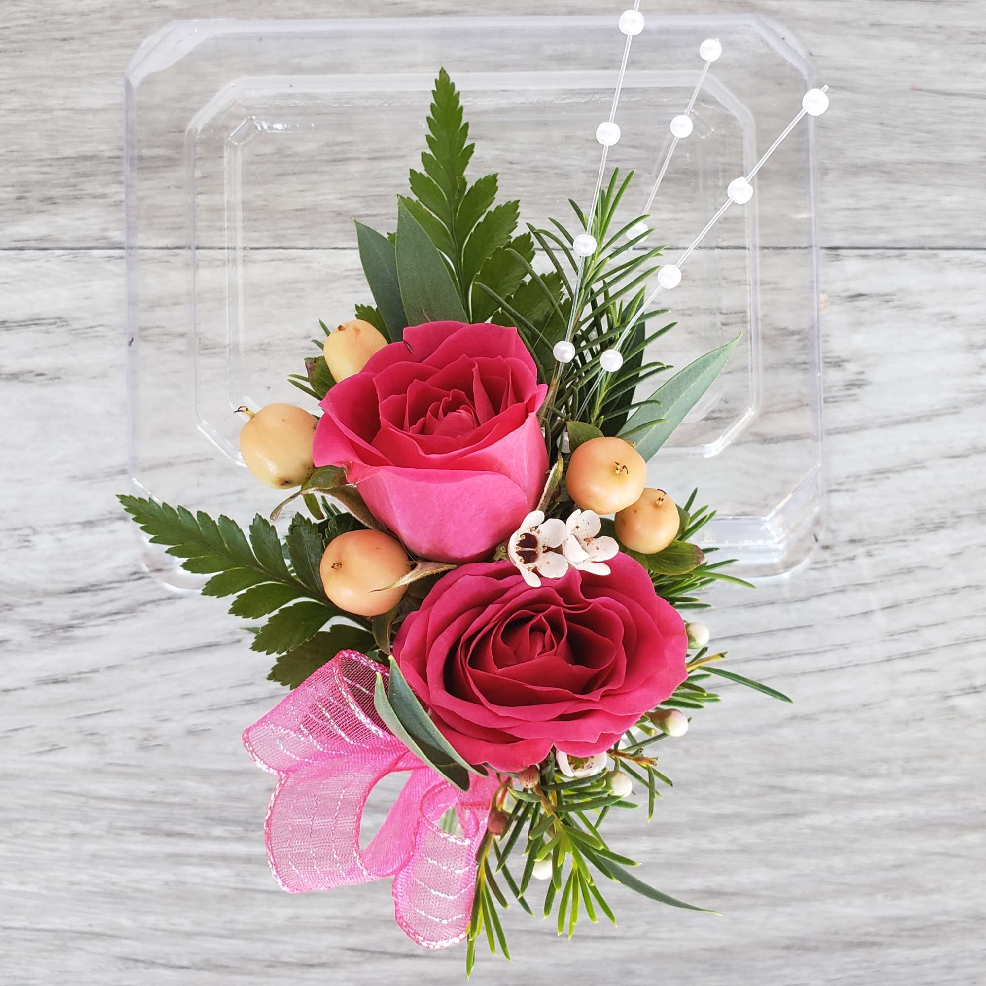 Two pink roses with berries and a pink ribbon on a clear tray