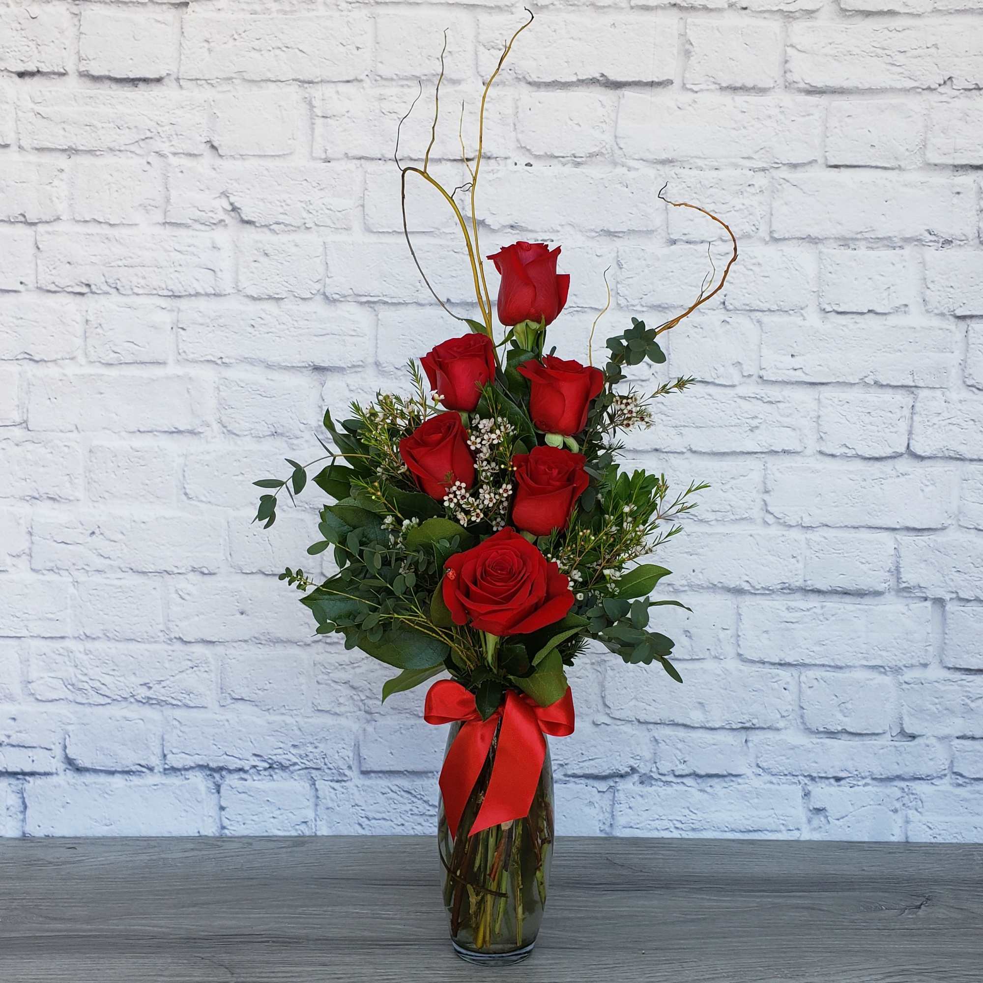 Red roses arranged in a glass vase with a red ribbon