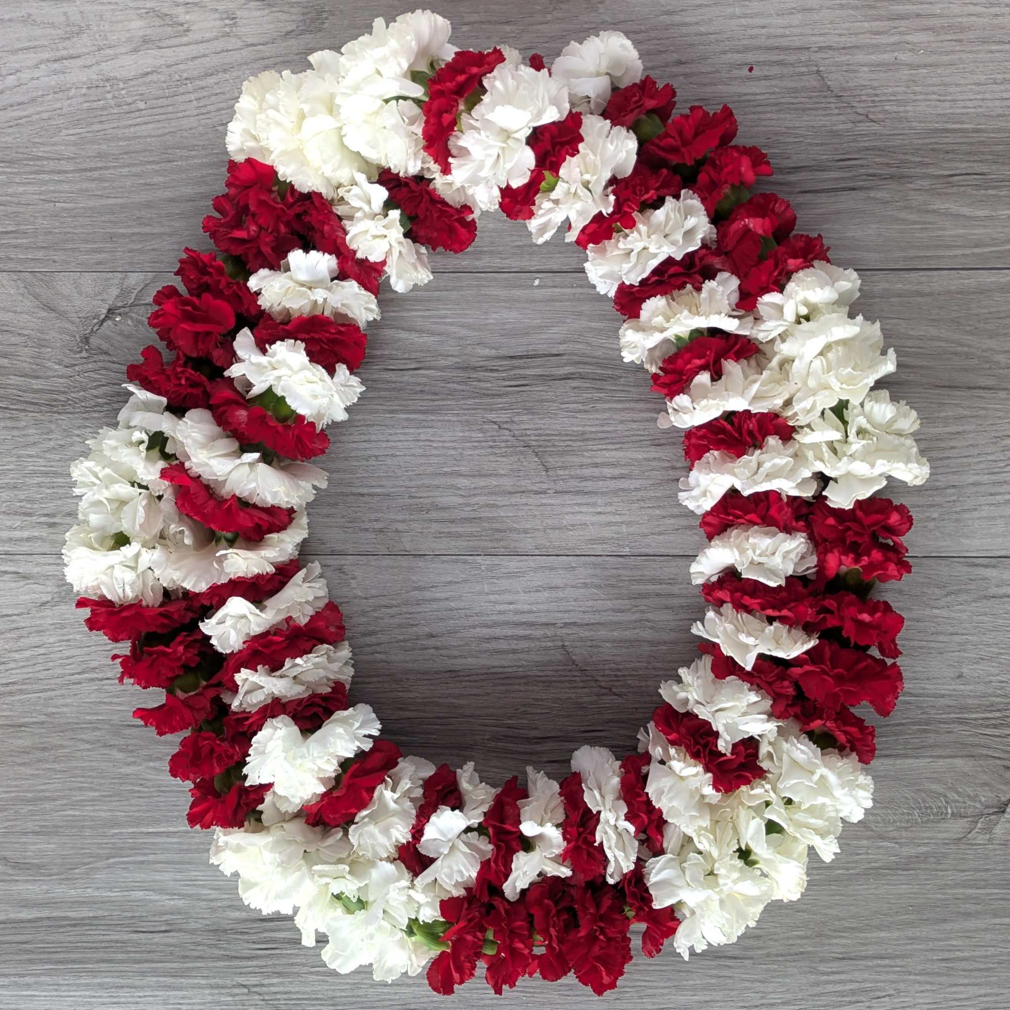 Red and white carnation lei arranged in a loop on a gray surface