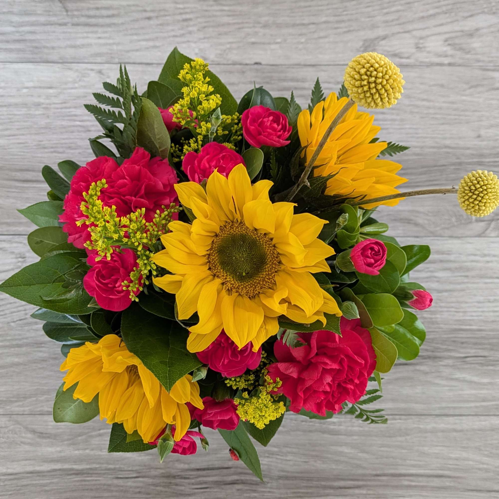 Bouquet of yellow sunflowers and hot pink carnations with greenery