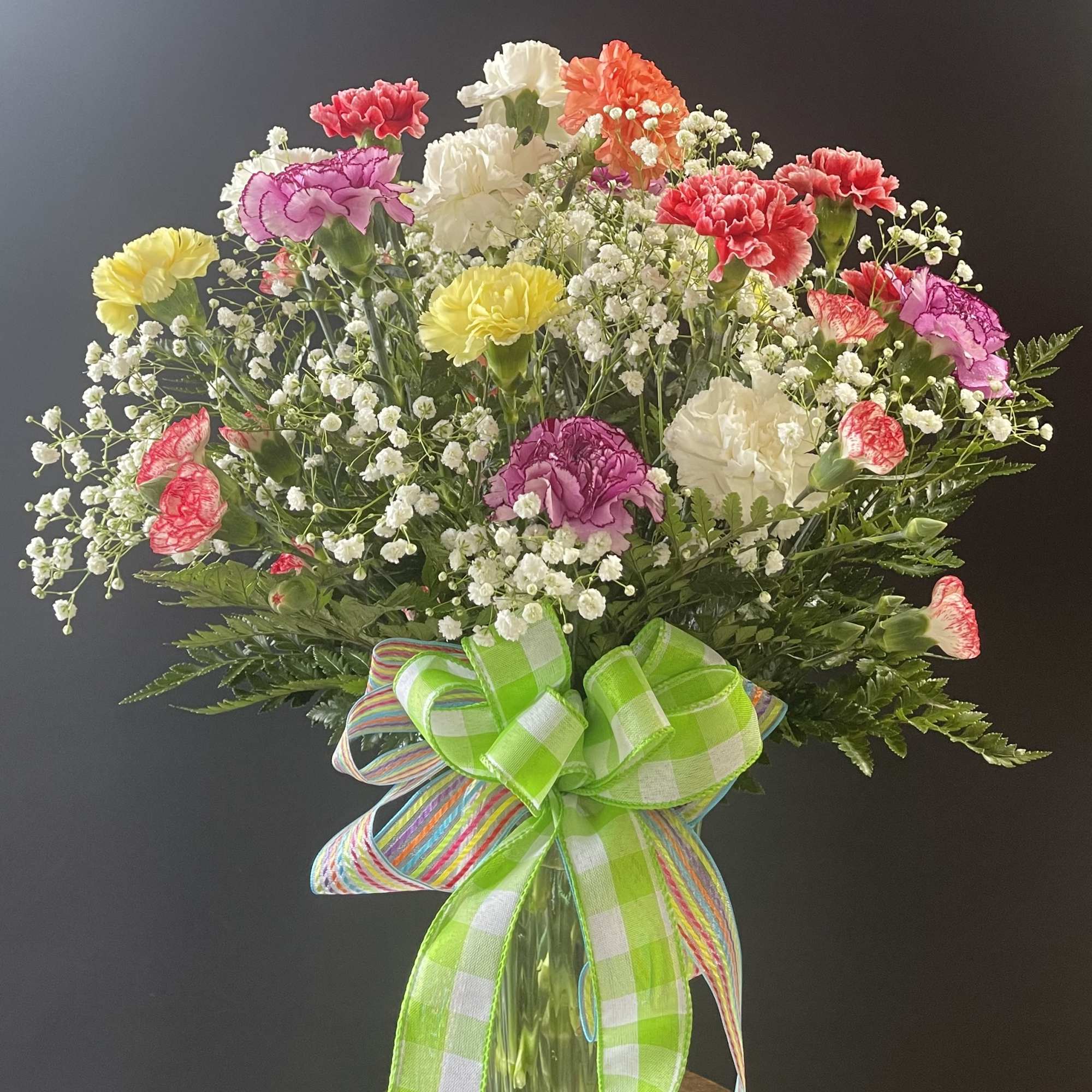 Colorful carnation bouquet in a glass vase with a large ribbon bow
