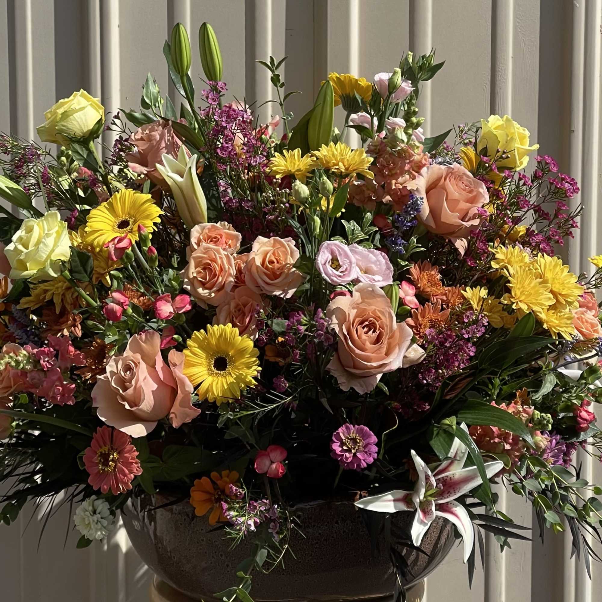 Large mixed bouquet with roses, lilies, and yellow daisies in a dark vase