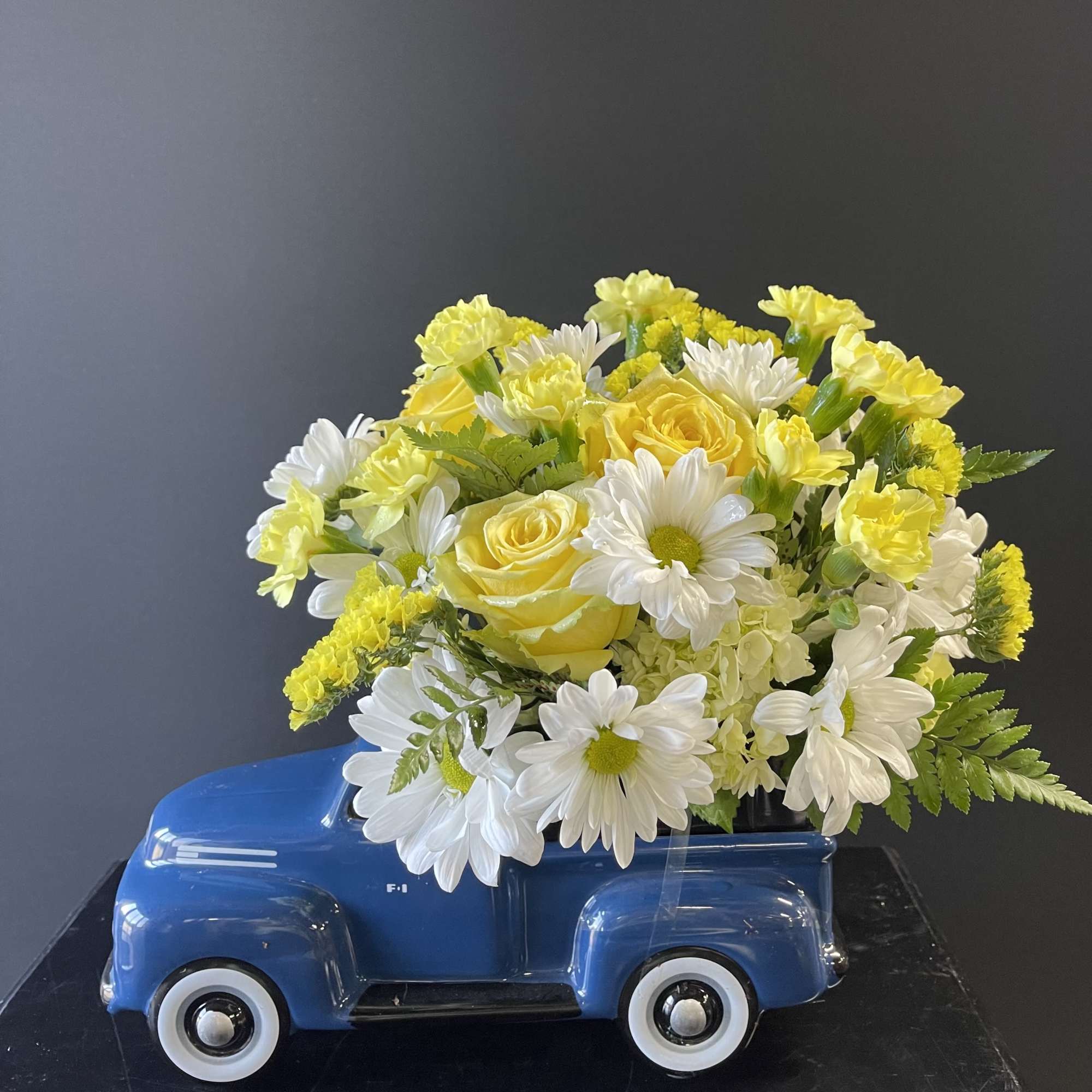 Yellow and white flower arrangement in a blue truck-shaped container