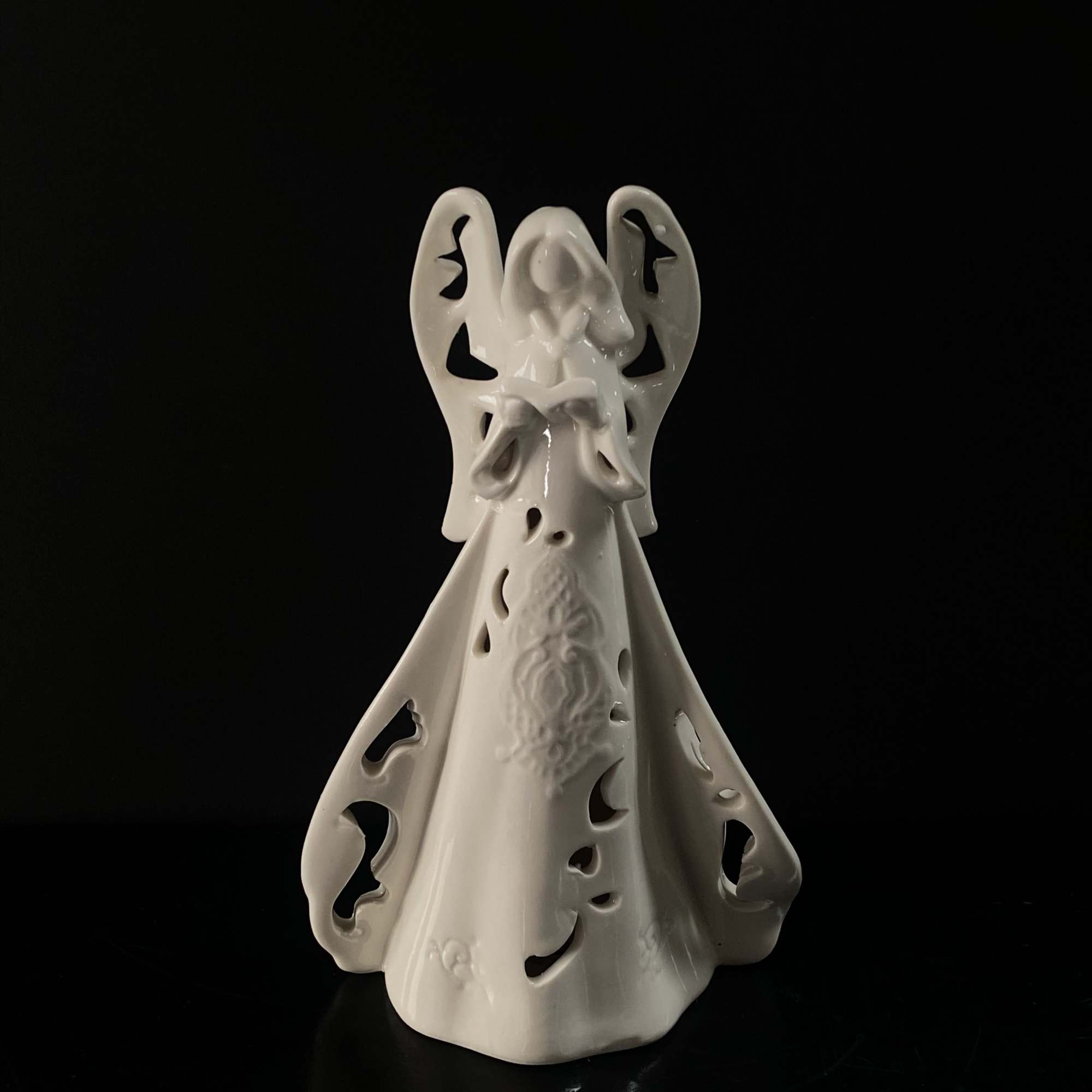 White ceramic angel figurine with cutout details on a black background