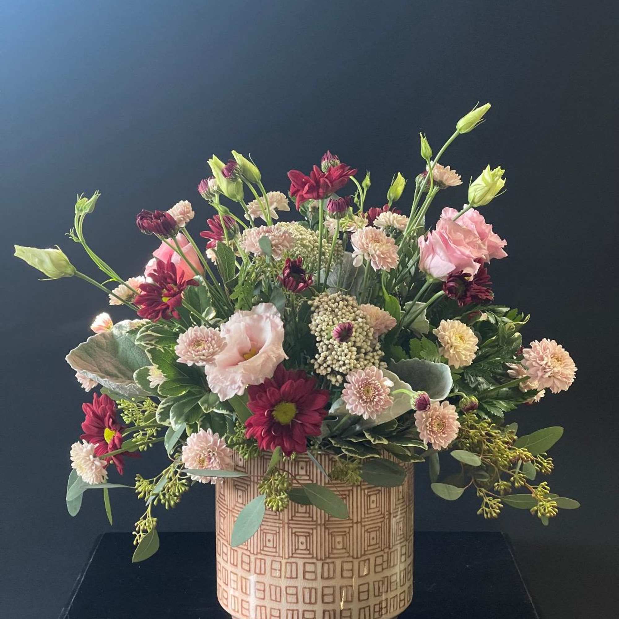 Mixed pink and burgundy flowers in a patterned ceramic vase